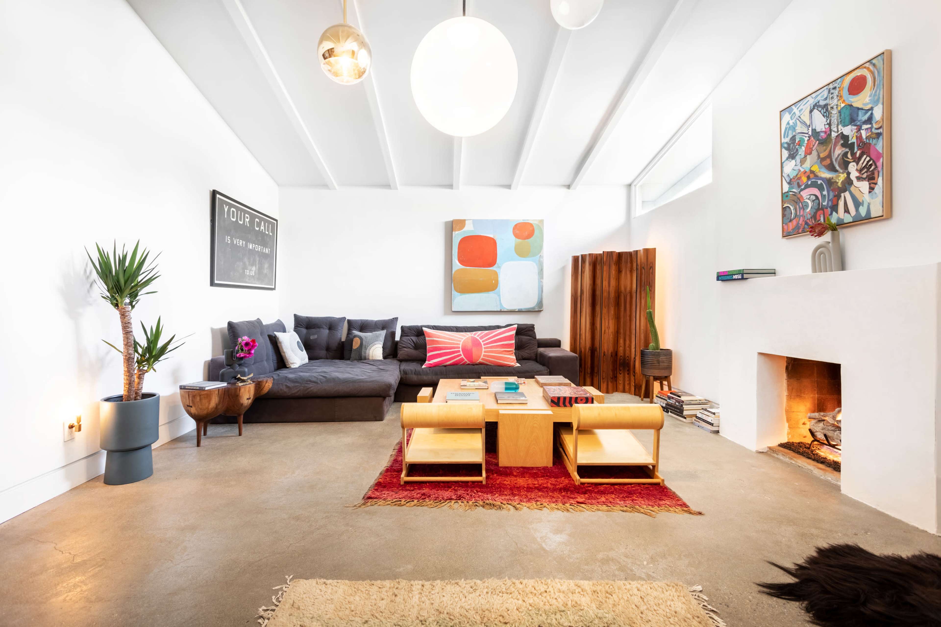 The image shows a modern living room featuring a large sectional sofa, a coffee table, a decorative rug, and a fireplace with artwork on the walls.
