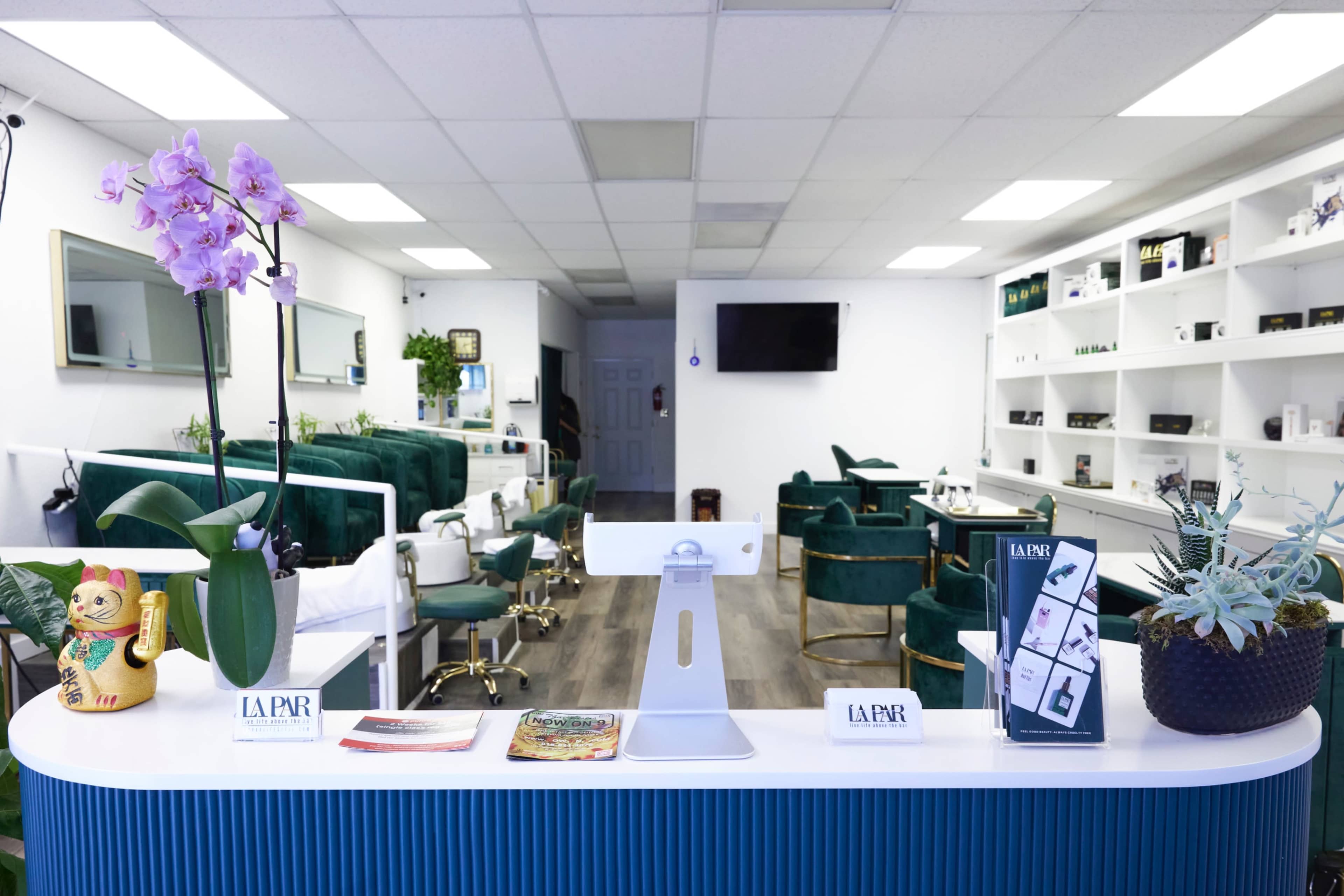 The image shows the interior of a salon with green upholstered chairs, a reception desk adorned with plants, and neatly arranged products on shelves.