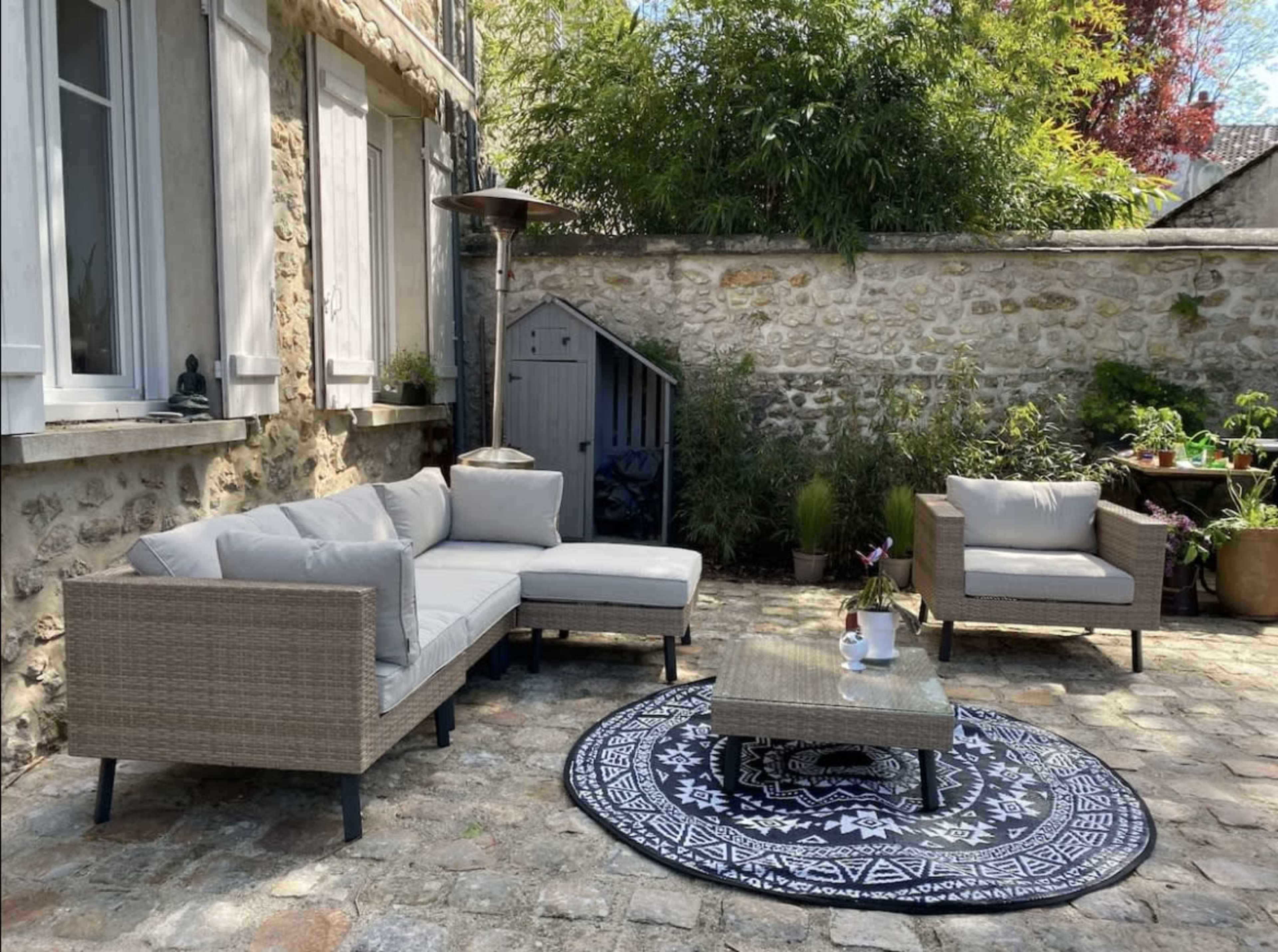 A cozy outdoor seating area with a sectional sofa, a coffee table, and greenery in a stone-paved courtyard.