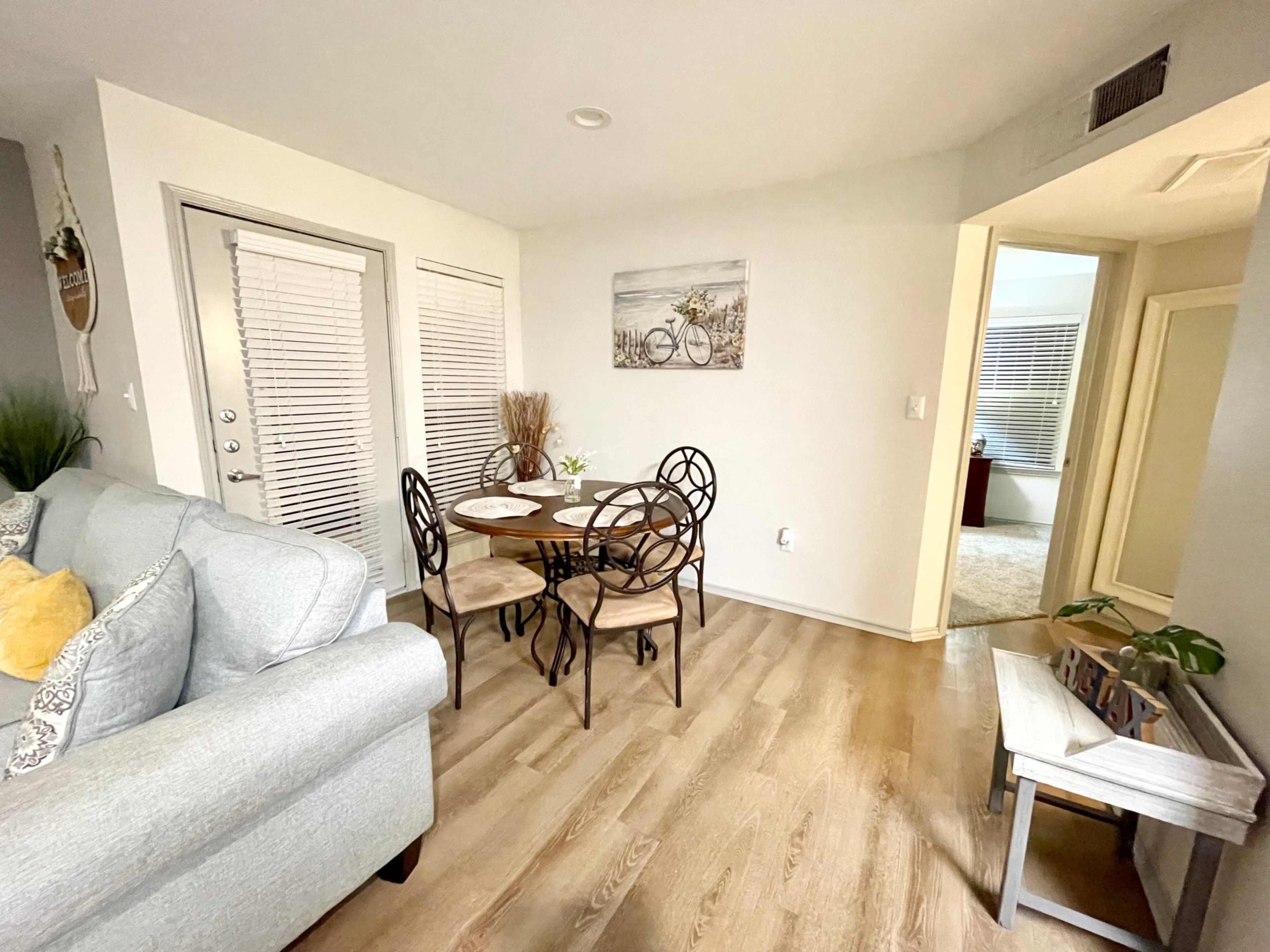 A small dining area with a round table and four chairs adjacent to a light-colored sofa and closed doors.