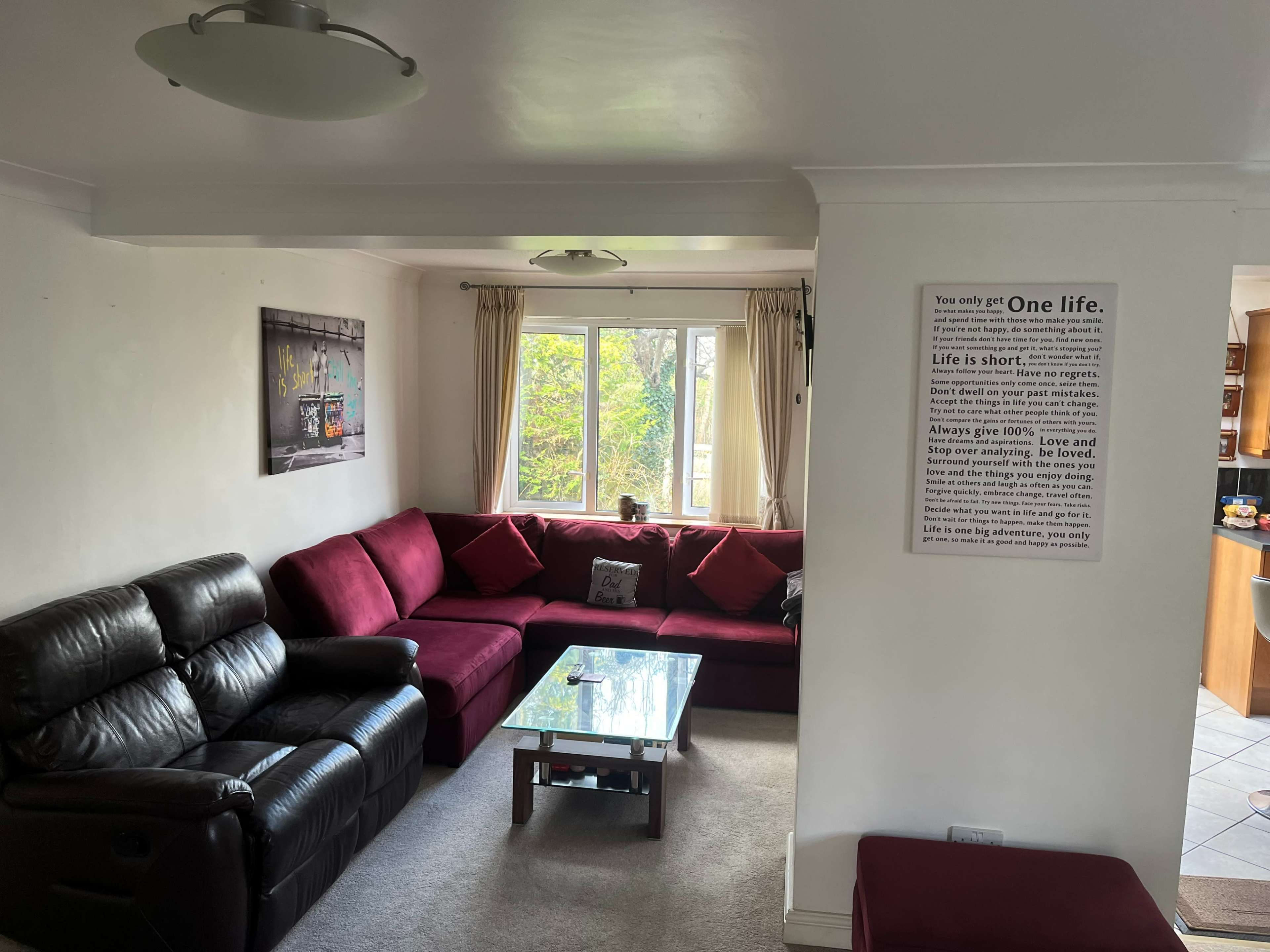 The living room features a sectional red sofa, a glass coffee table, and a wall hanging with motivational text.