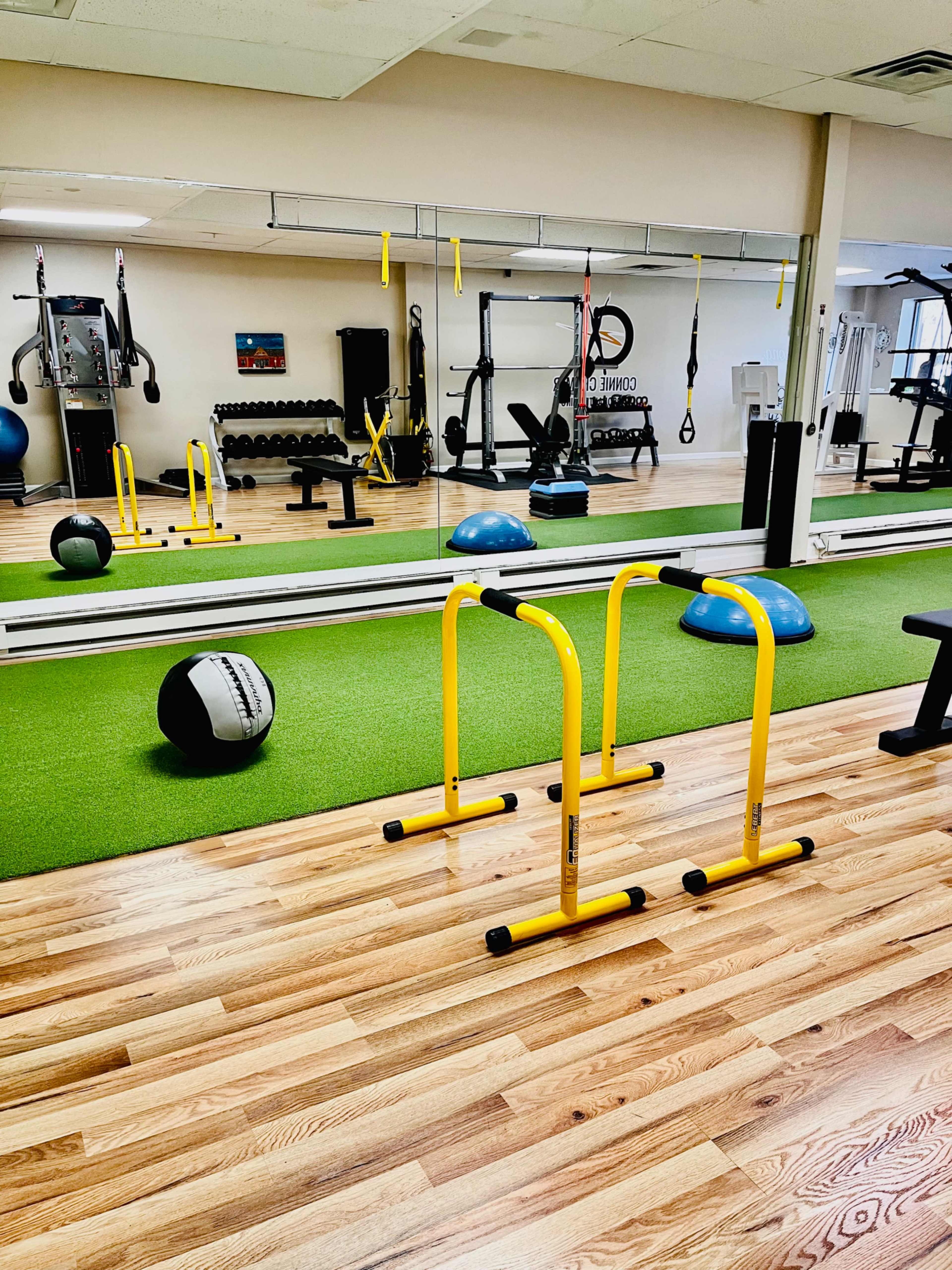 A gym interior features yellow parallel bars, exercise equipment, and a mirrored wall on a green turf surface.