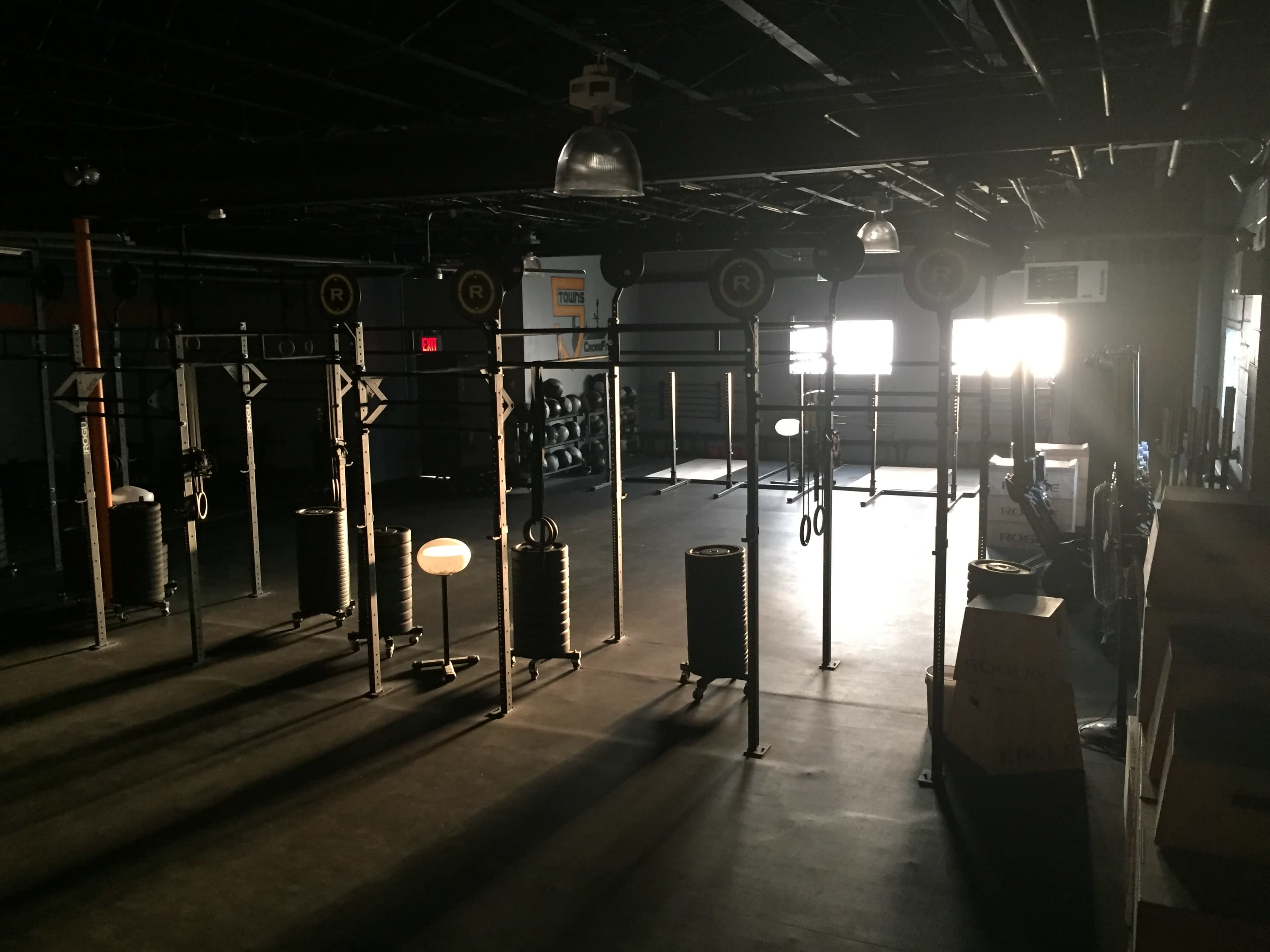 The image shows a dimly lit gym with multiple weightlifting stations and equipment arranged in a spacious area.