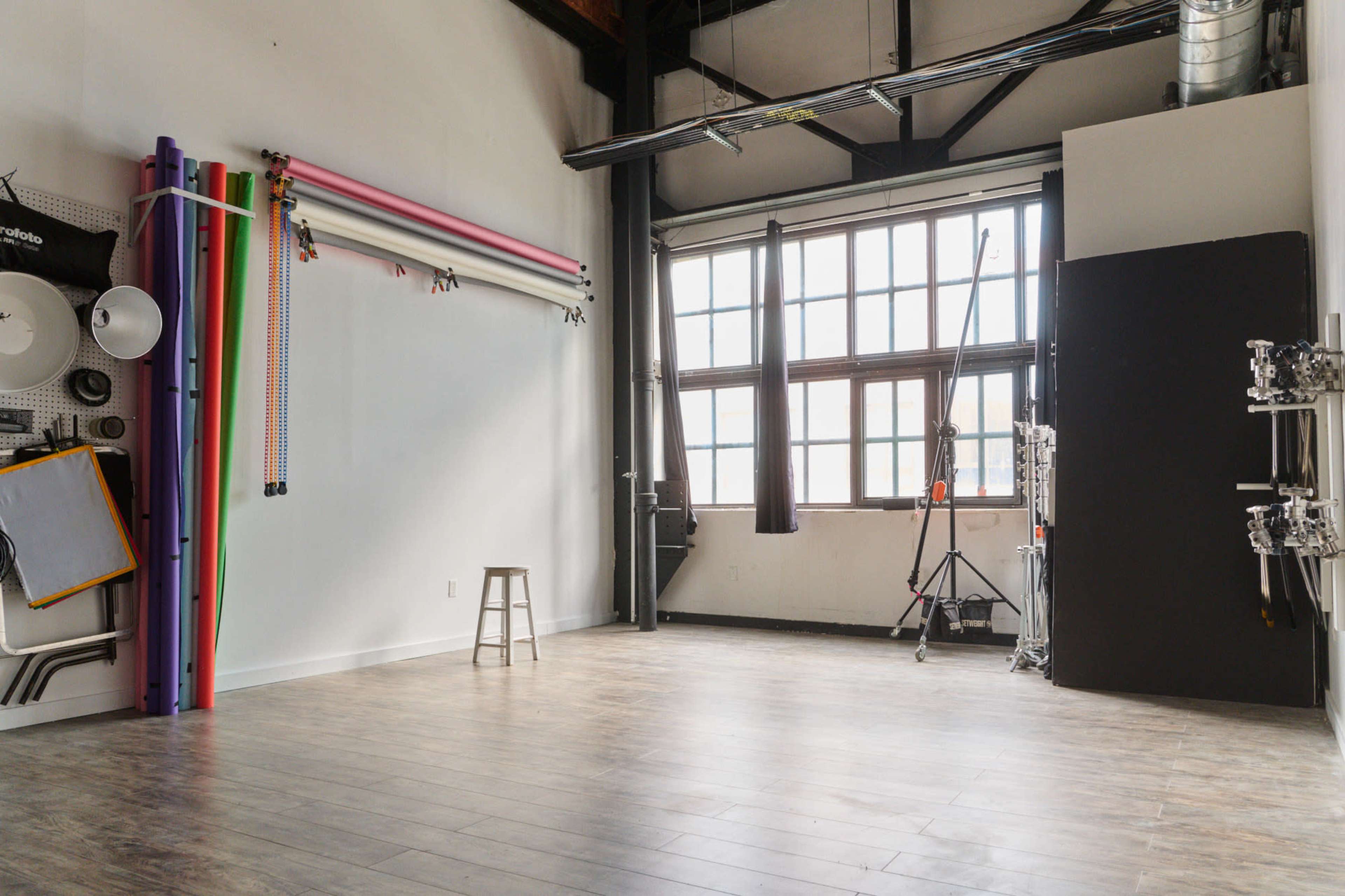 An empty photography studio with colorful backdrops on one wall and large windows allowing natural light in.