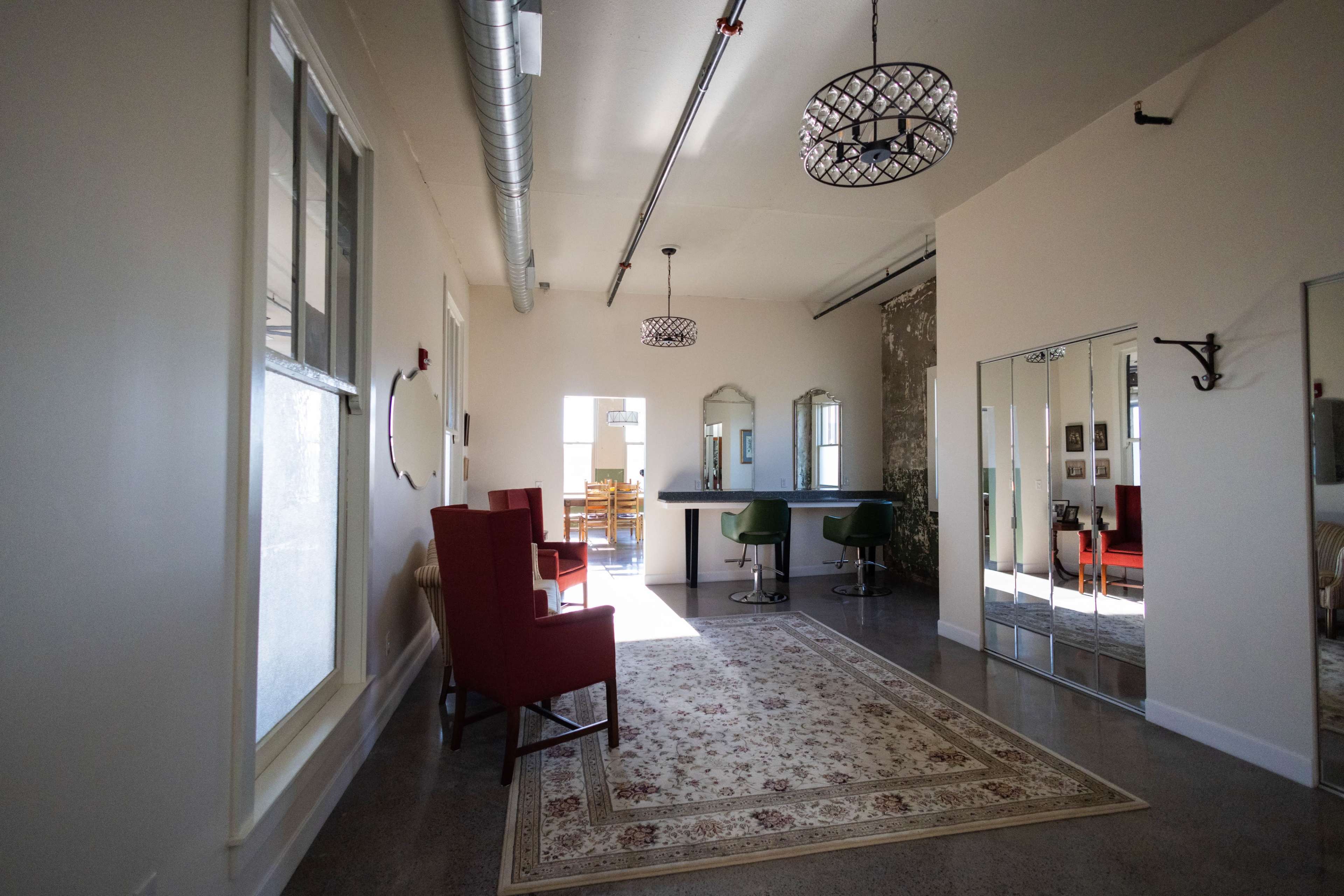 A well-lit hallway featuring two red chairs, a mirrored wall, and a small bar area with green stools.
