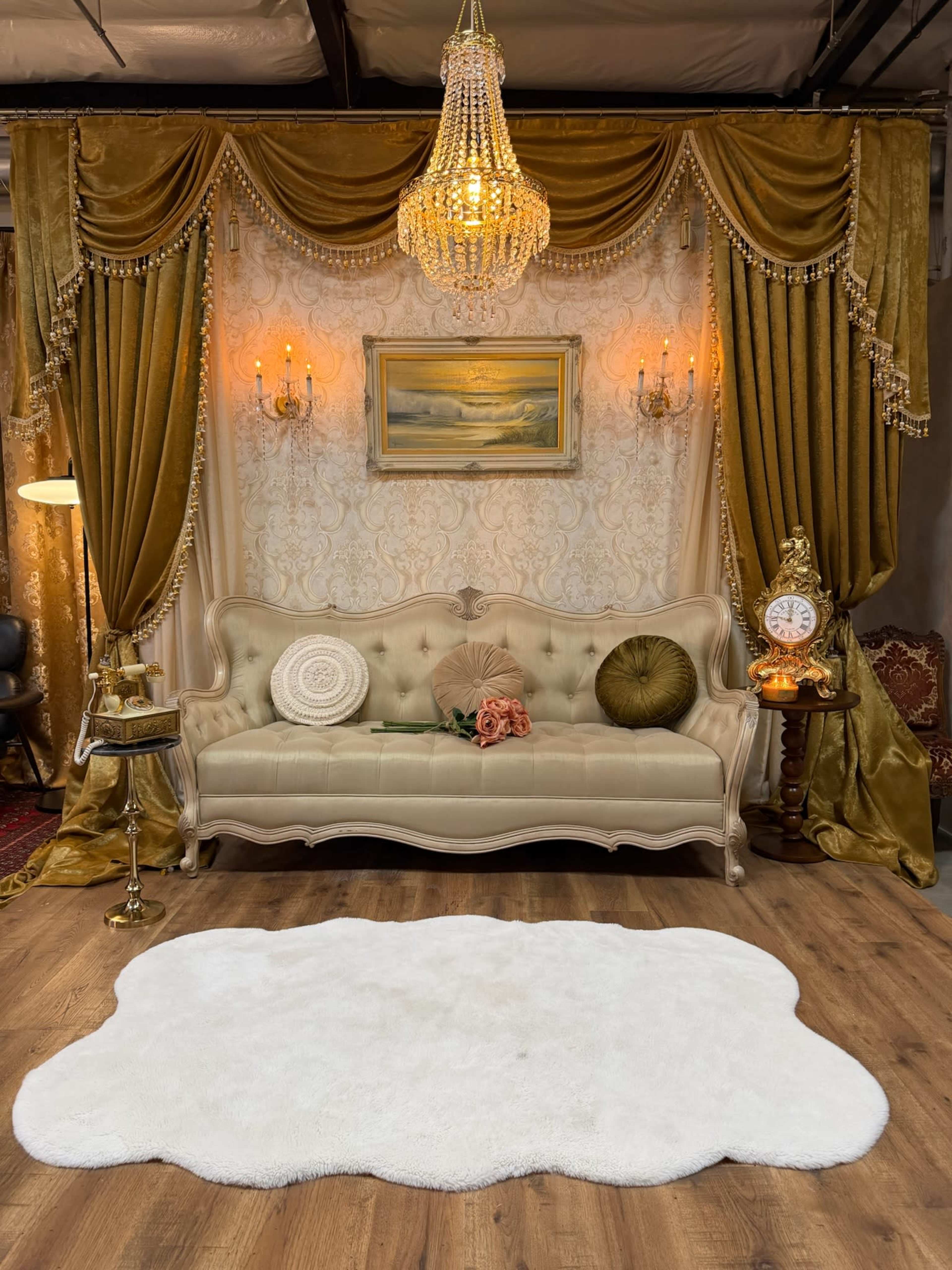 The image features an elegantly styled interior with a cream-colored couch, decorative drapery, a chandelier, and a plush area rug.
