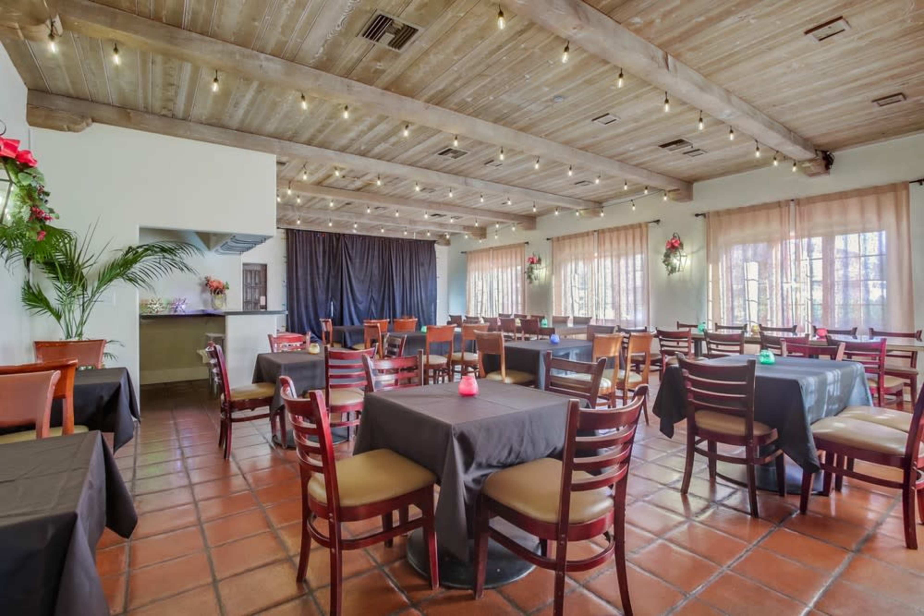 The image shows a dining area in a restaurant with wooden beams, tables covered in black cloth, and a softly lit ambiance.