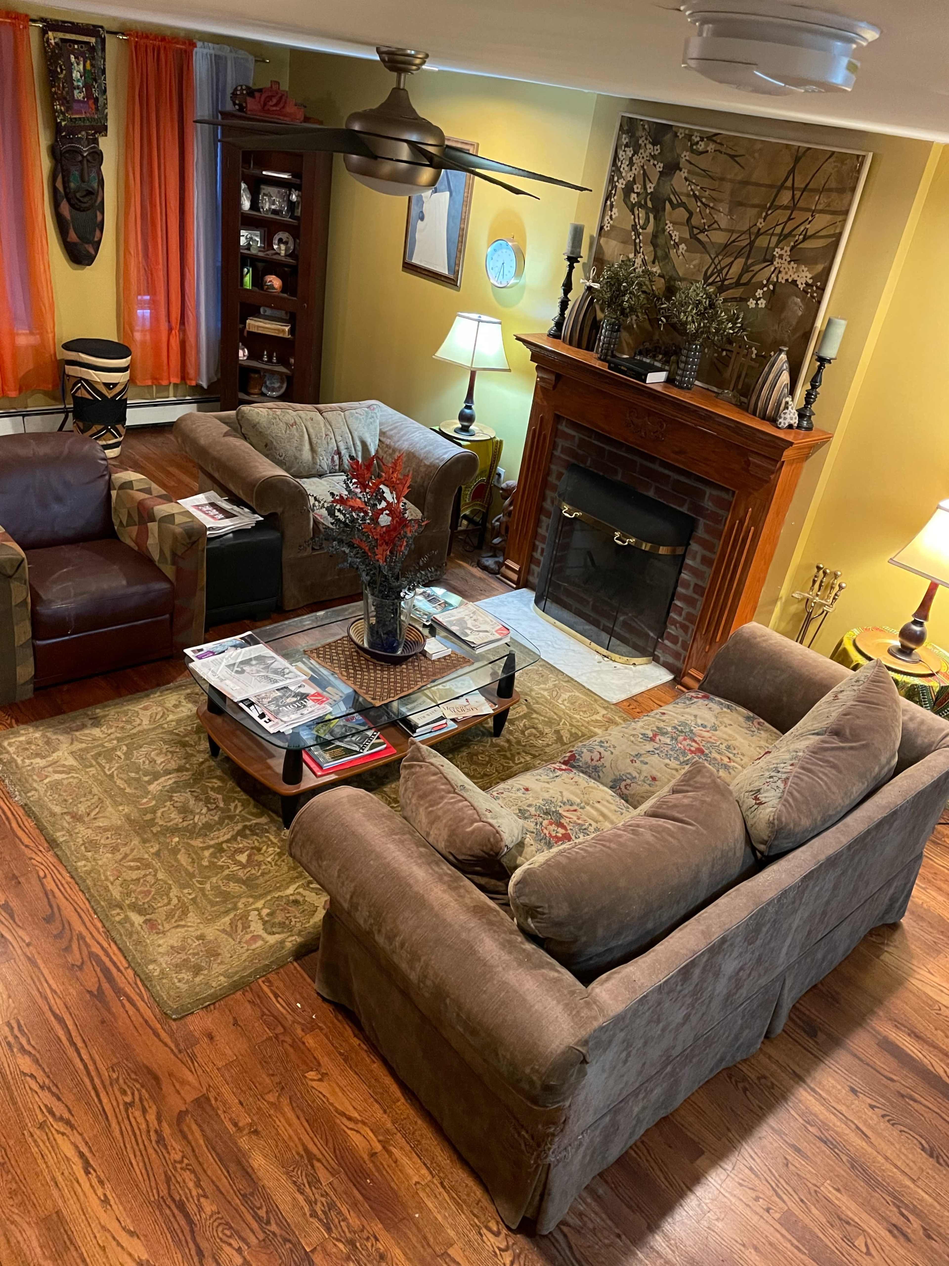 The image shows a cozy living room with two sofas, a coffee table covered in magazines, a fireplace, and decorative elements on the walls.