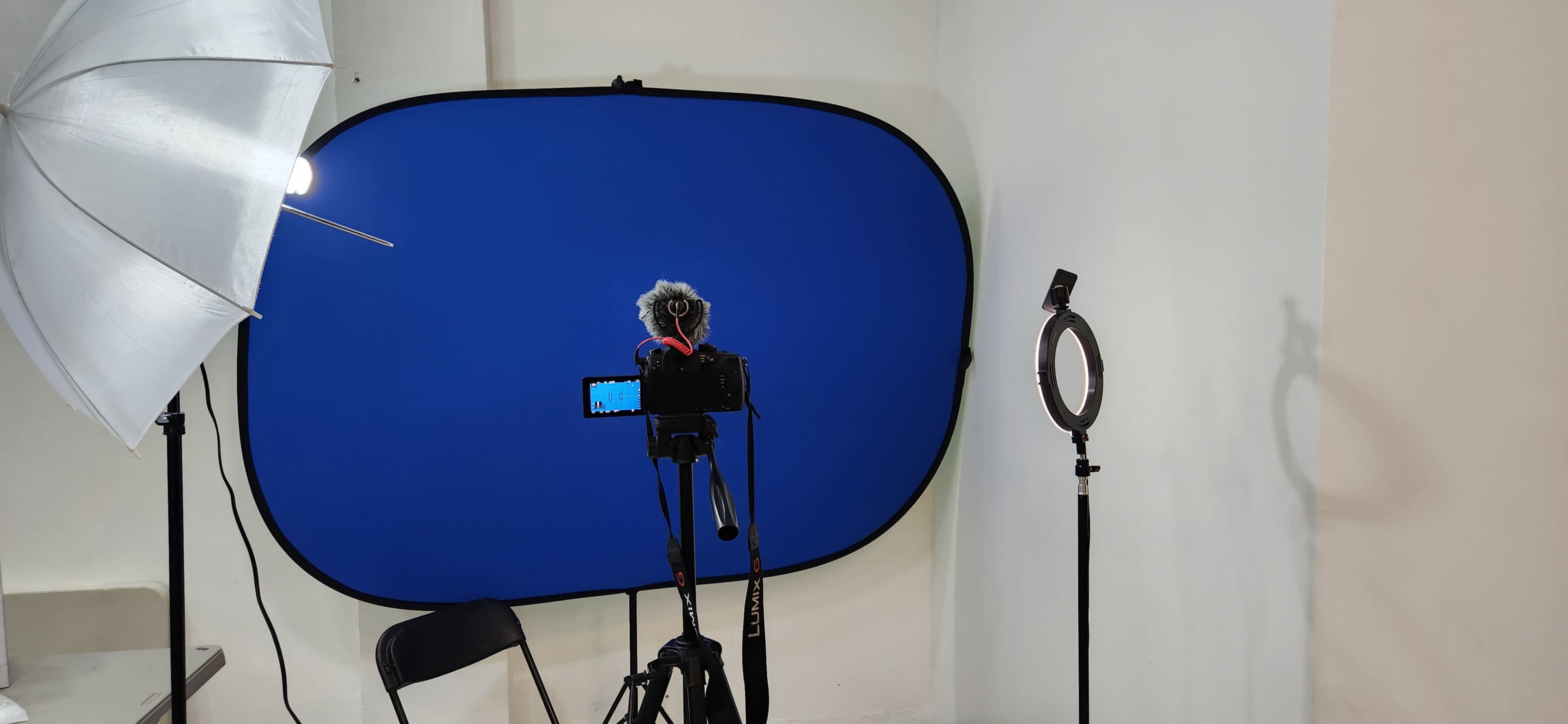 A photography setup with a blue backdrop, a camera on a tripod, a microphone, and lighting equipment.