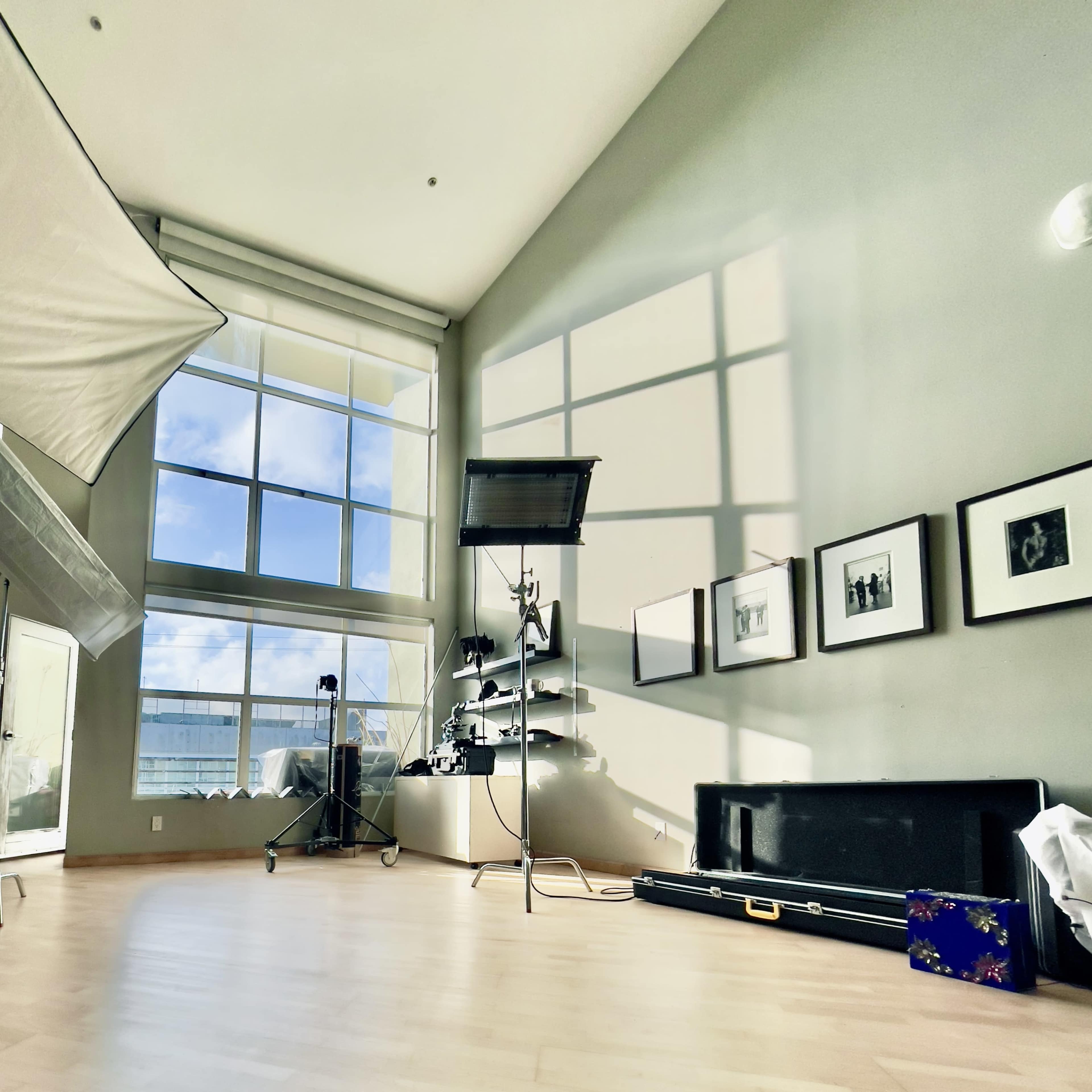 A spacious room with large windows, a lighting setup, and various framed photographs on the wall.