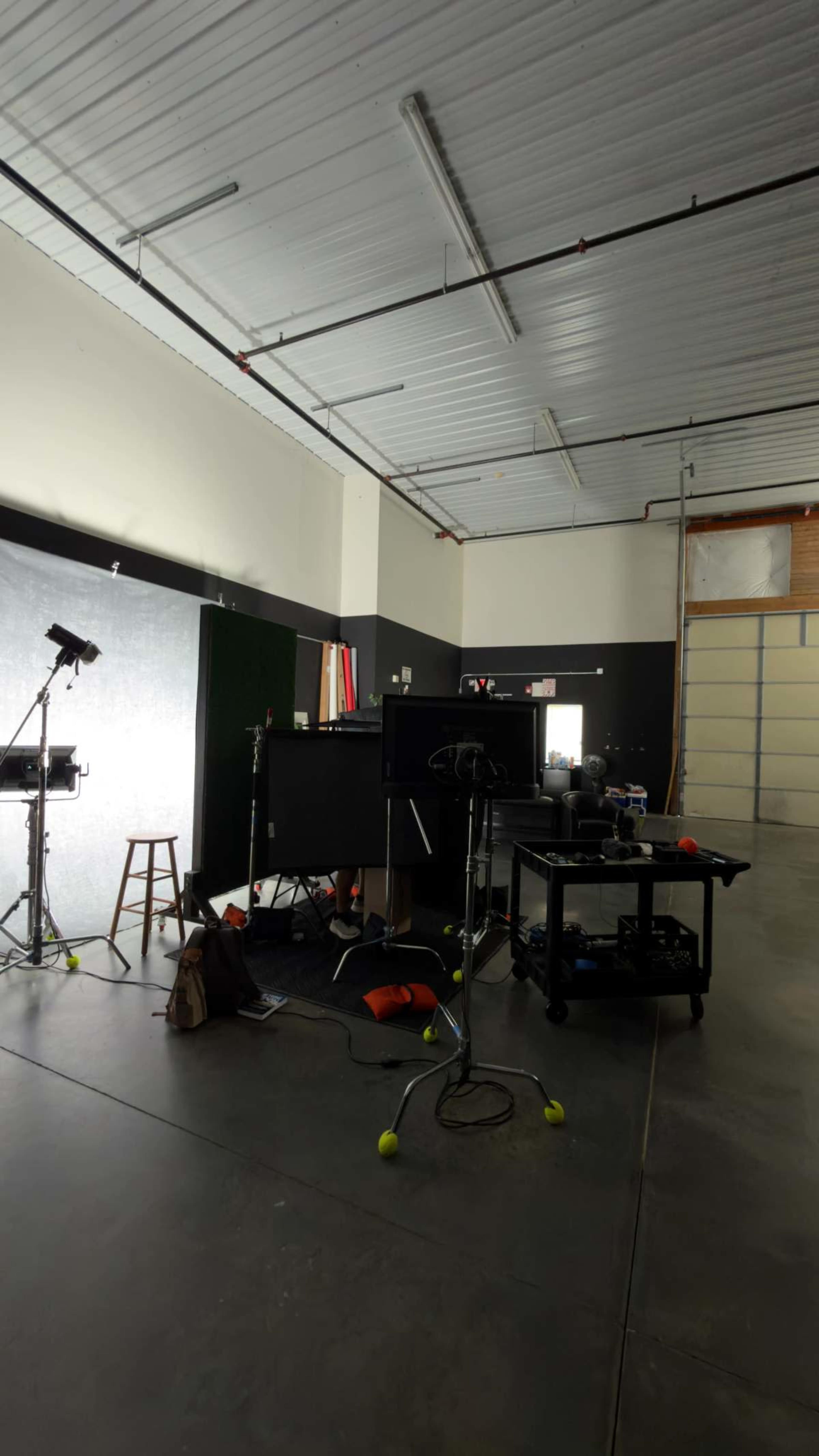 The image shows an indoor studio space with various equipment, including lighting, cameras, and a stool, arranged around a dark backdrop.