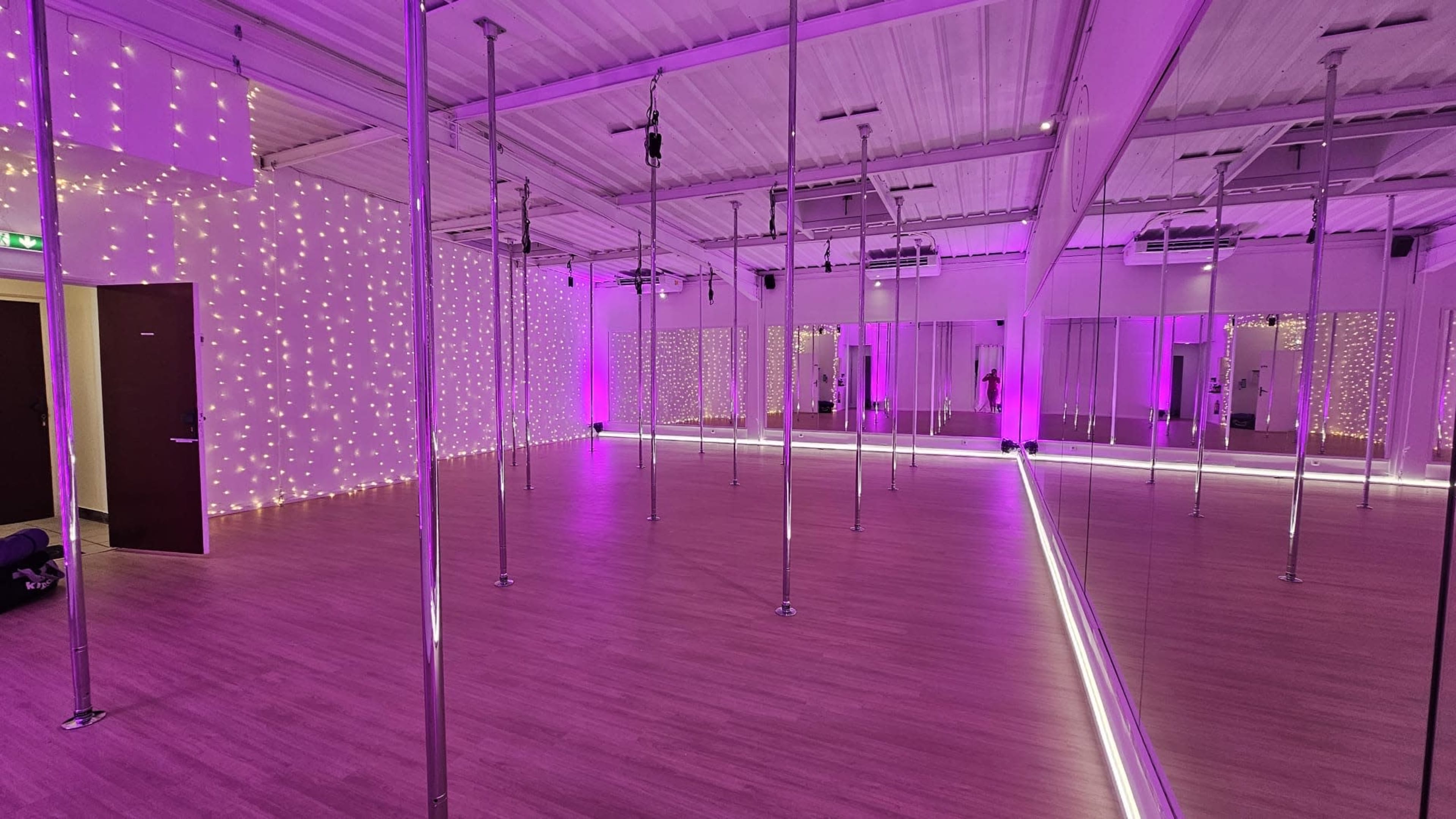 A brightly lit pole dancing studio with mirrored walls and purple ambient lighting.