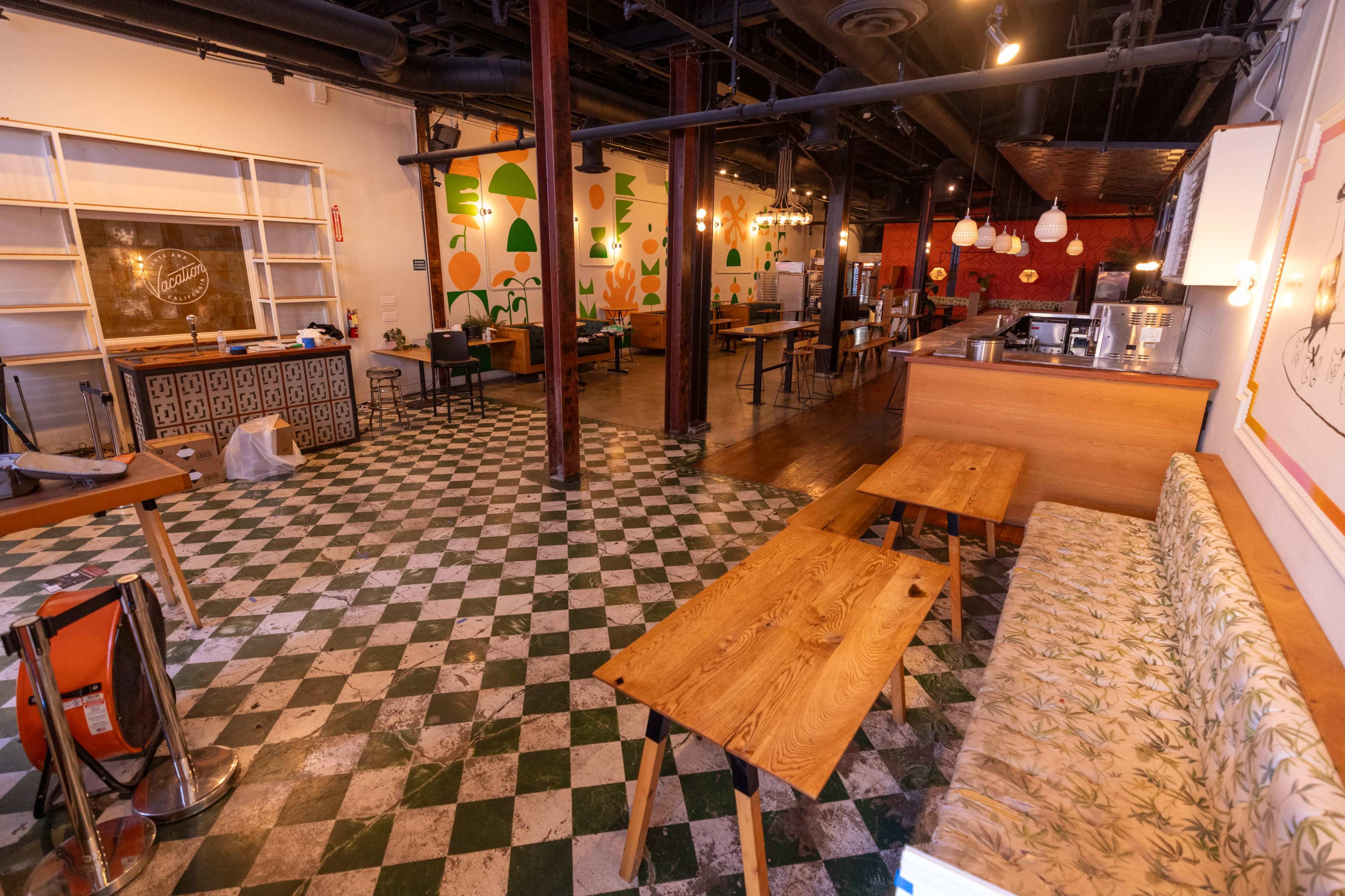 The image shows an interior of a café with a checkered tile floor, wooden tables, and vibrant wall murals featuring abstract shapes.