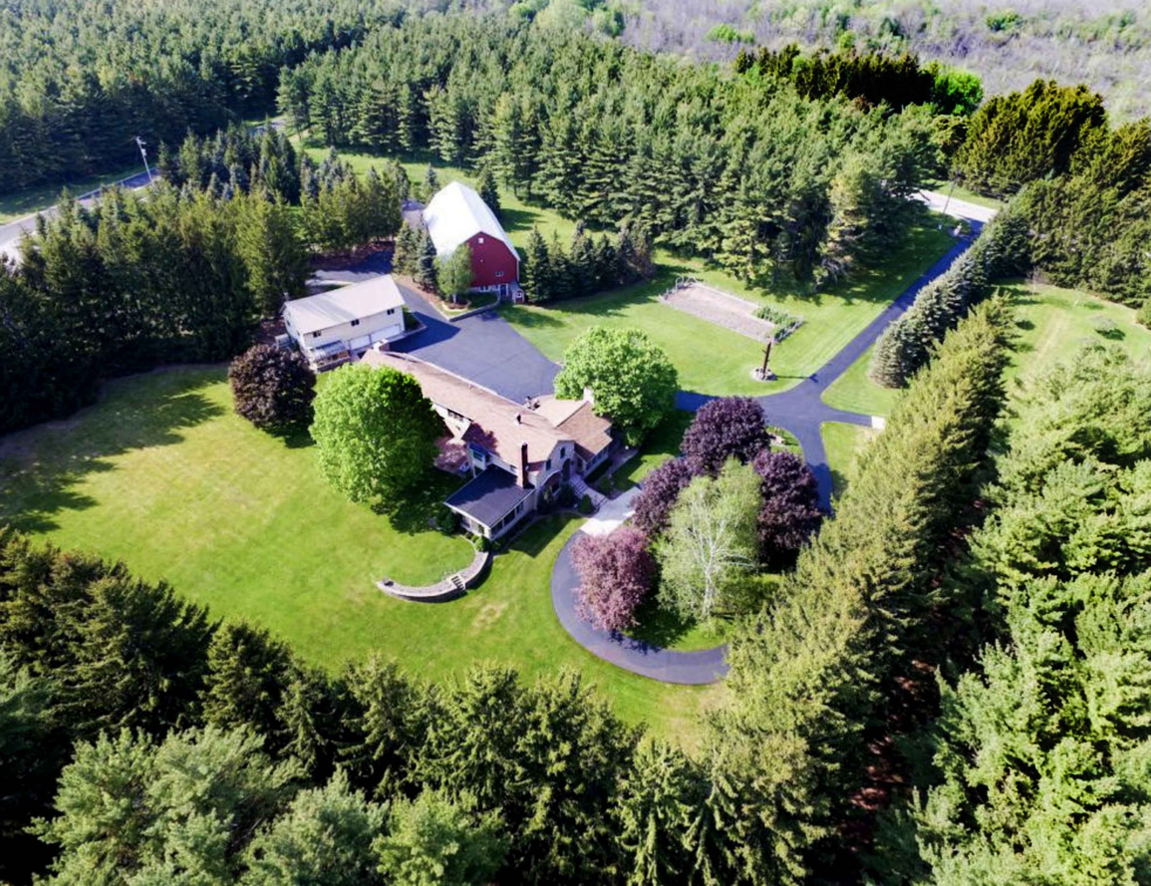 An aerial view of a large property with a main house, a barn, and several trees surrounding a well-maintained lawn.