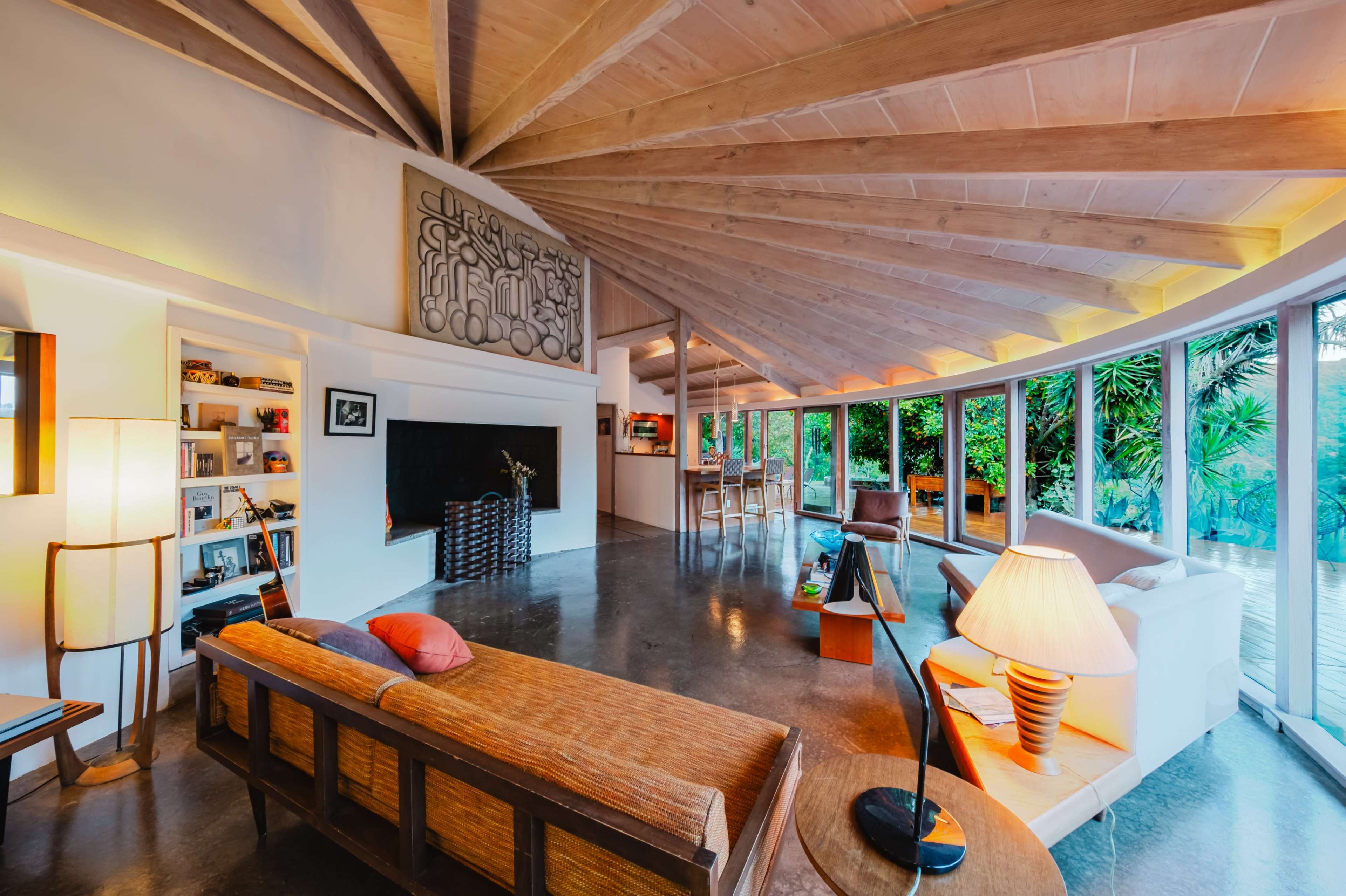 The image shows a modern living room with a wooden ceiling, large windows, a fireplace, and a mix of seating areas.