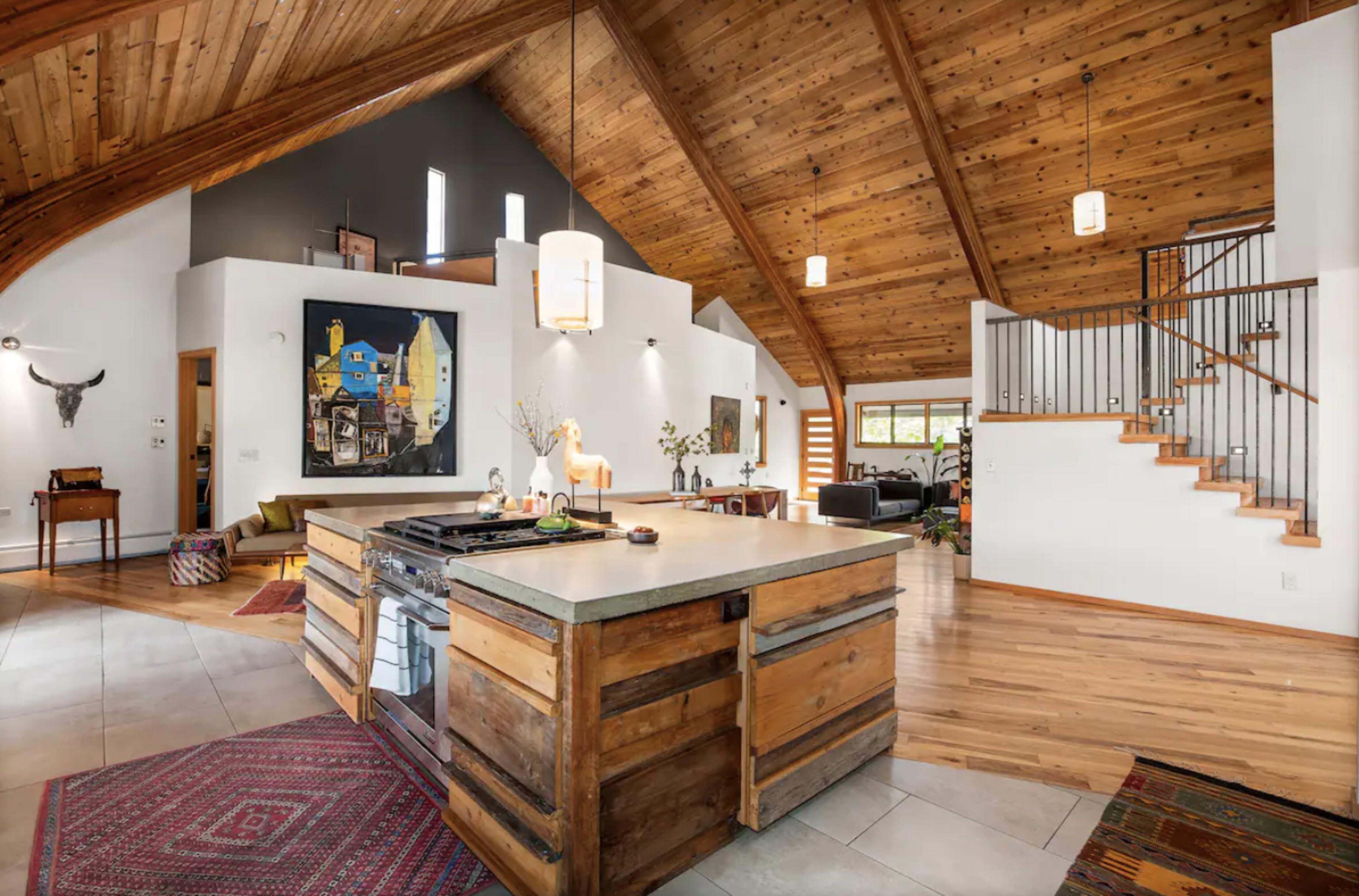A spacious kitchen with a wooden island, high vaulted ceilings, and a staircase leading to an upper level.