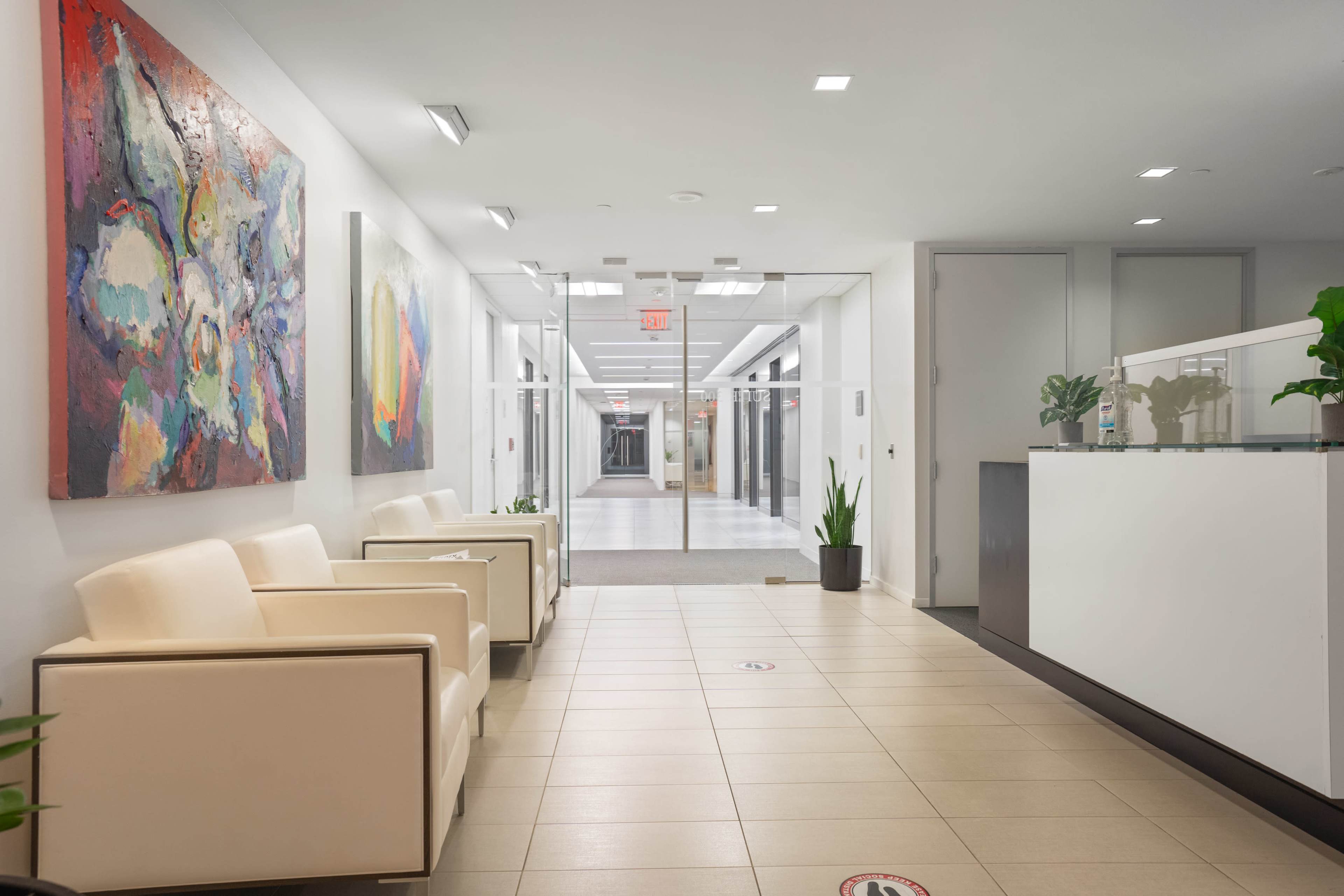 A modern reception area with white chairs, colorful artwork on the walls, and a minimalist front desk.