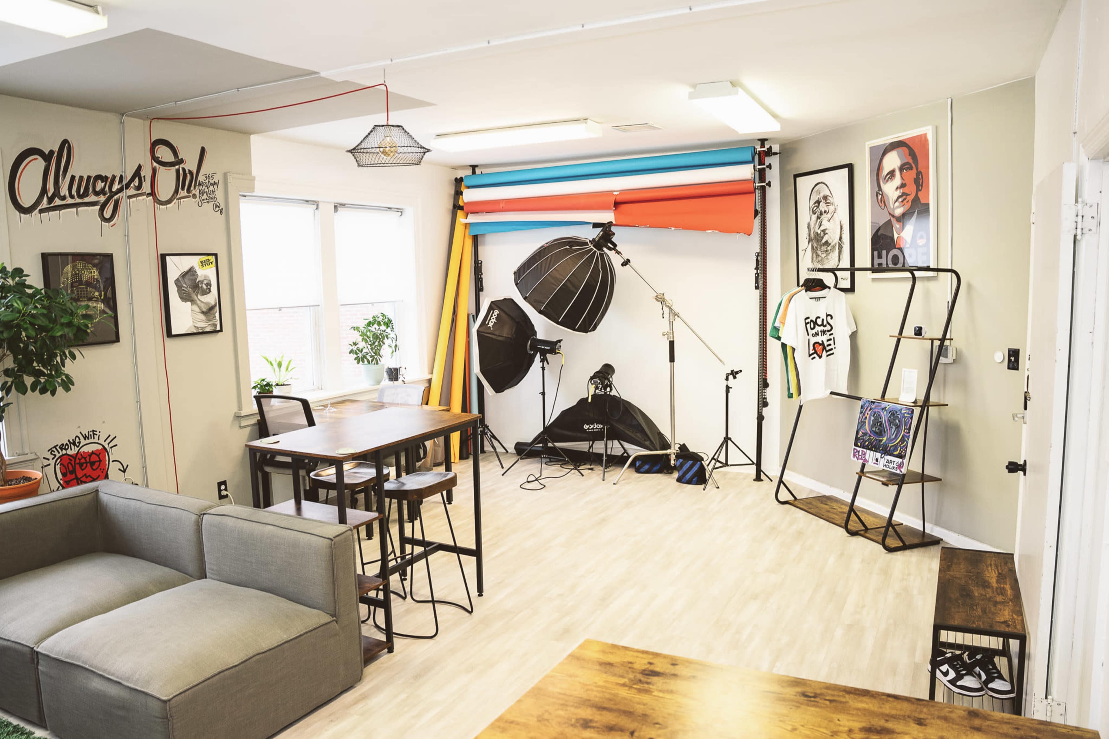 A well-lit studio space featuring a seating area, photography equipment with backdrops, and artwork displayed on the walls.