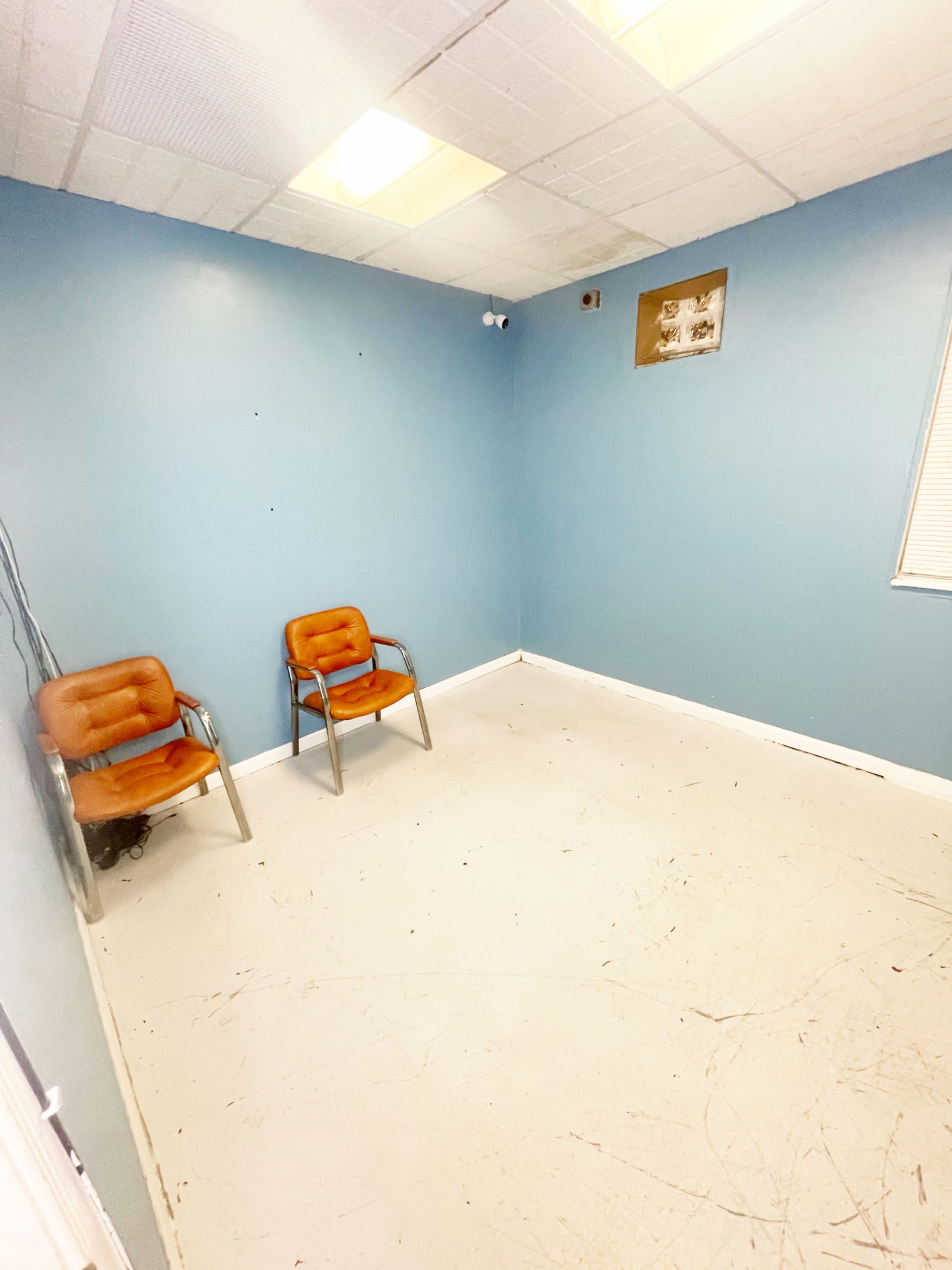 A sparsely furnished room features two brown chairs against a blue wall, with a small window and a ceiling light.