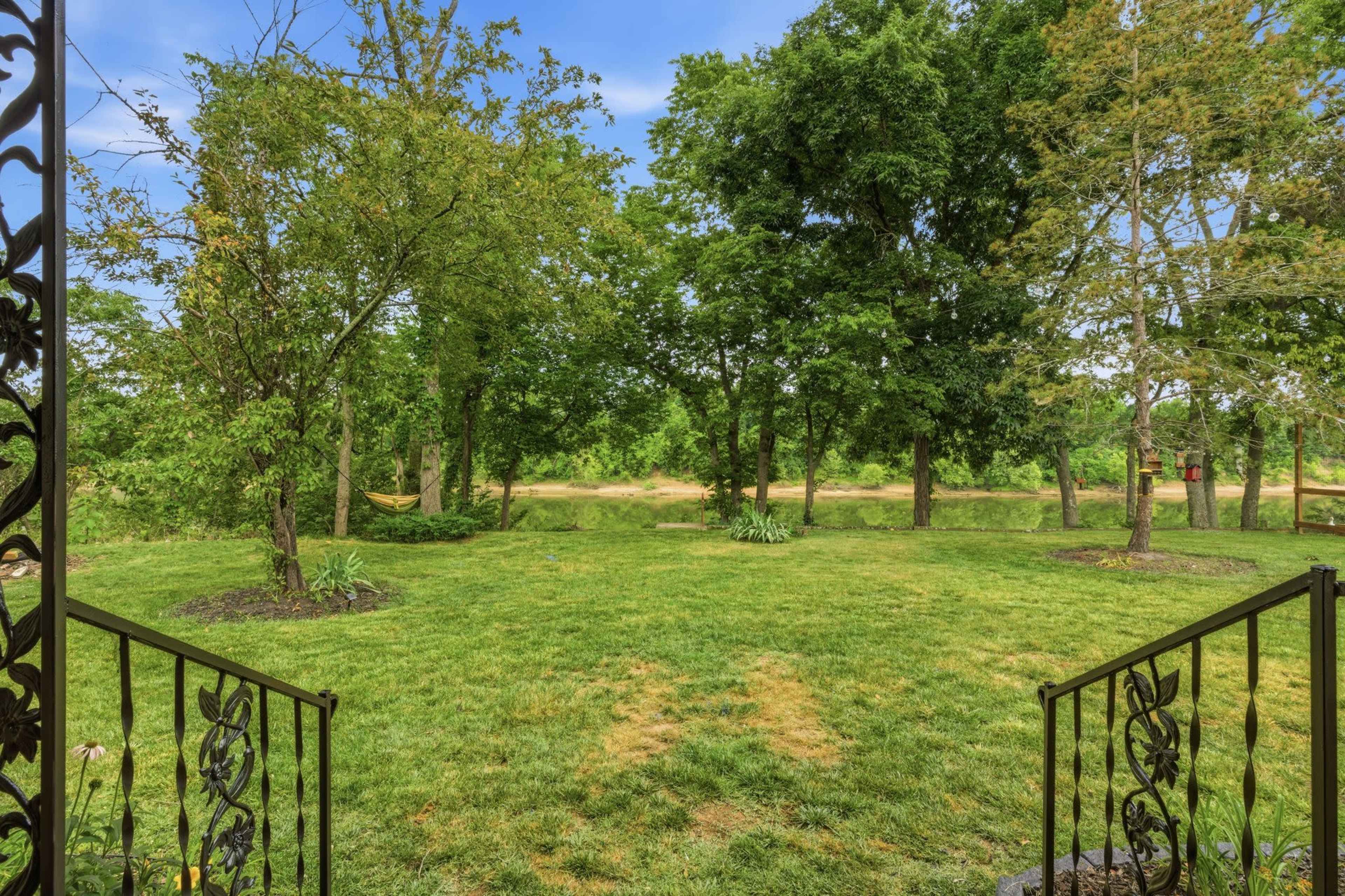 The image shows a grassy yard framed by trees, leading to a body of water in the background.