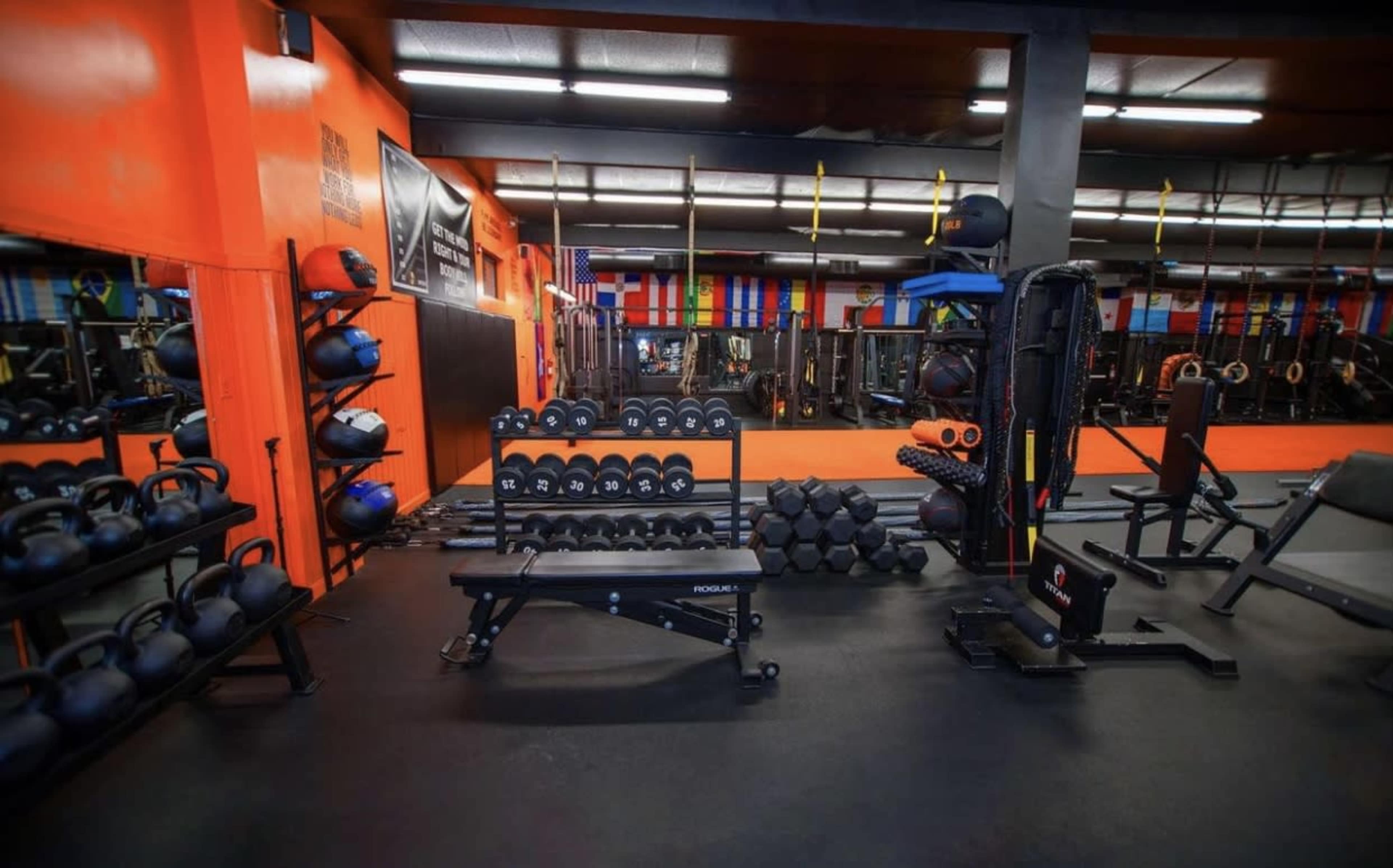 A fitness gym with various weights, kettlebells, and exercise equipment arranged on the floor against brightly colored walls and mirrors.