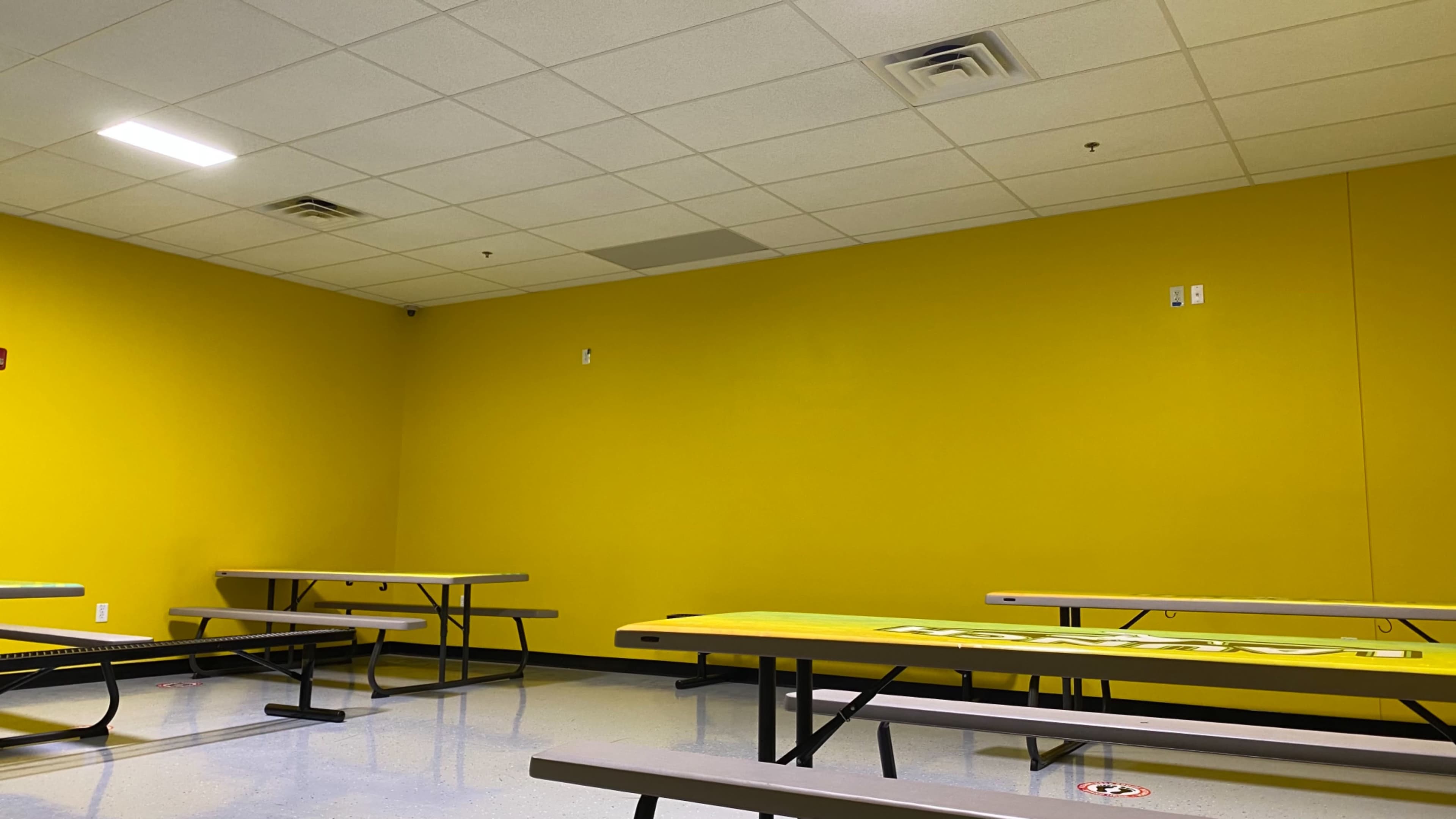 A room with bright yellow walls, several gray tables, and a linoleum floor.