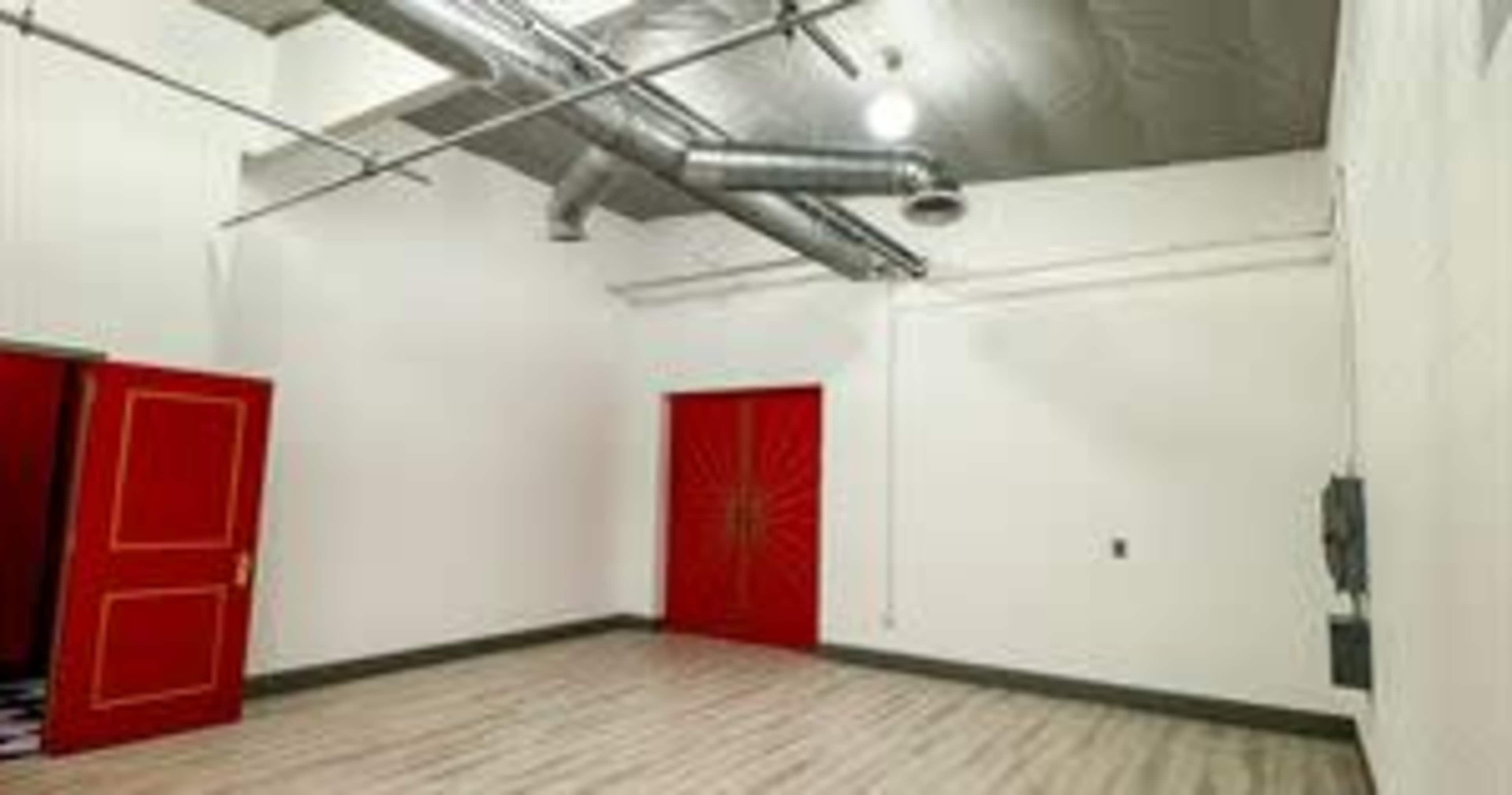 An empty room with white walls, a wooden floor, and a red door on one side.