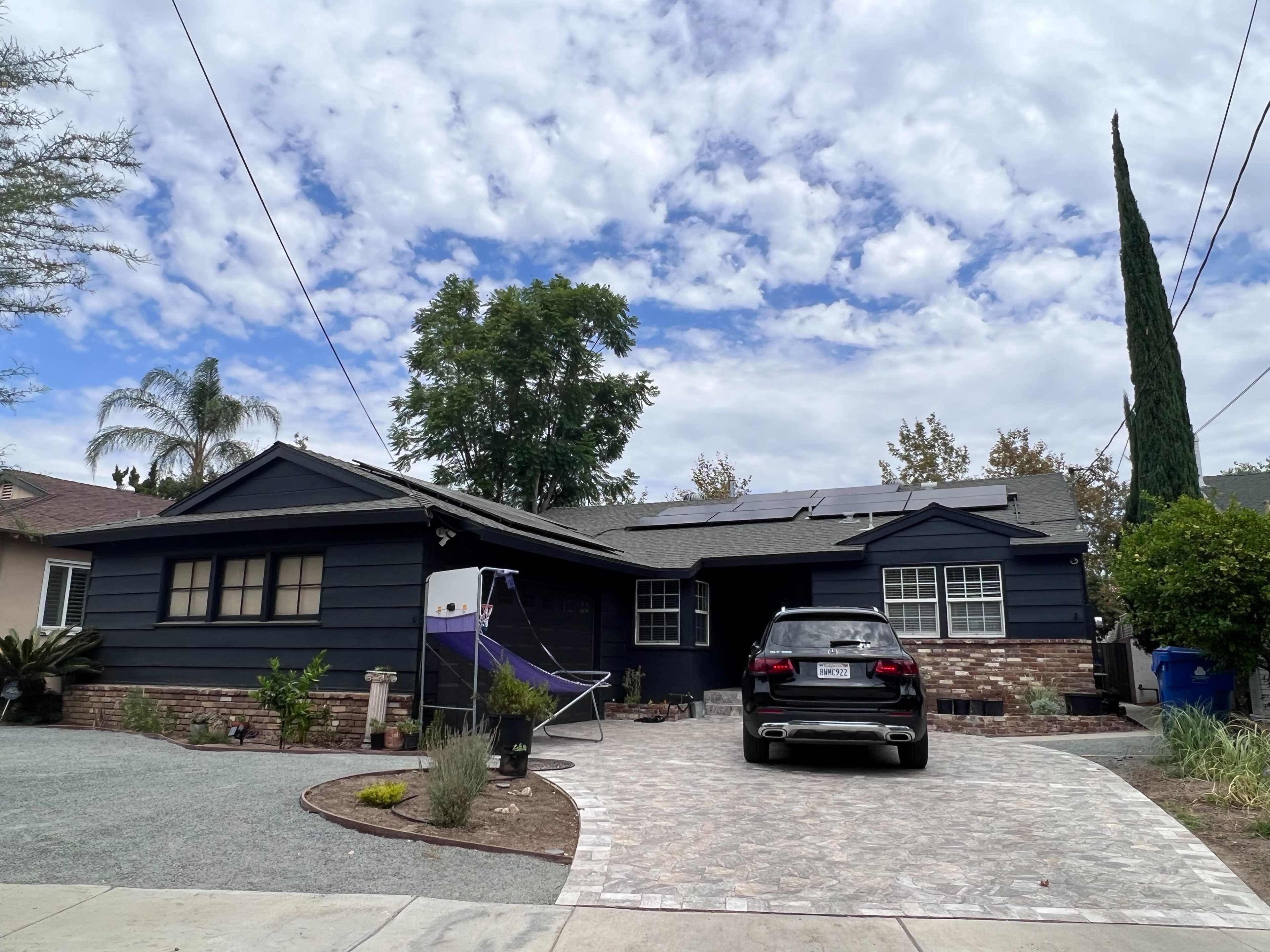 A dark-painted house with solar panels on the roof, a paved driveway, and a car parked in front.