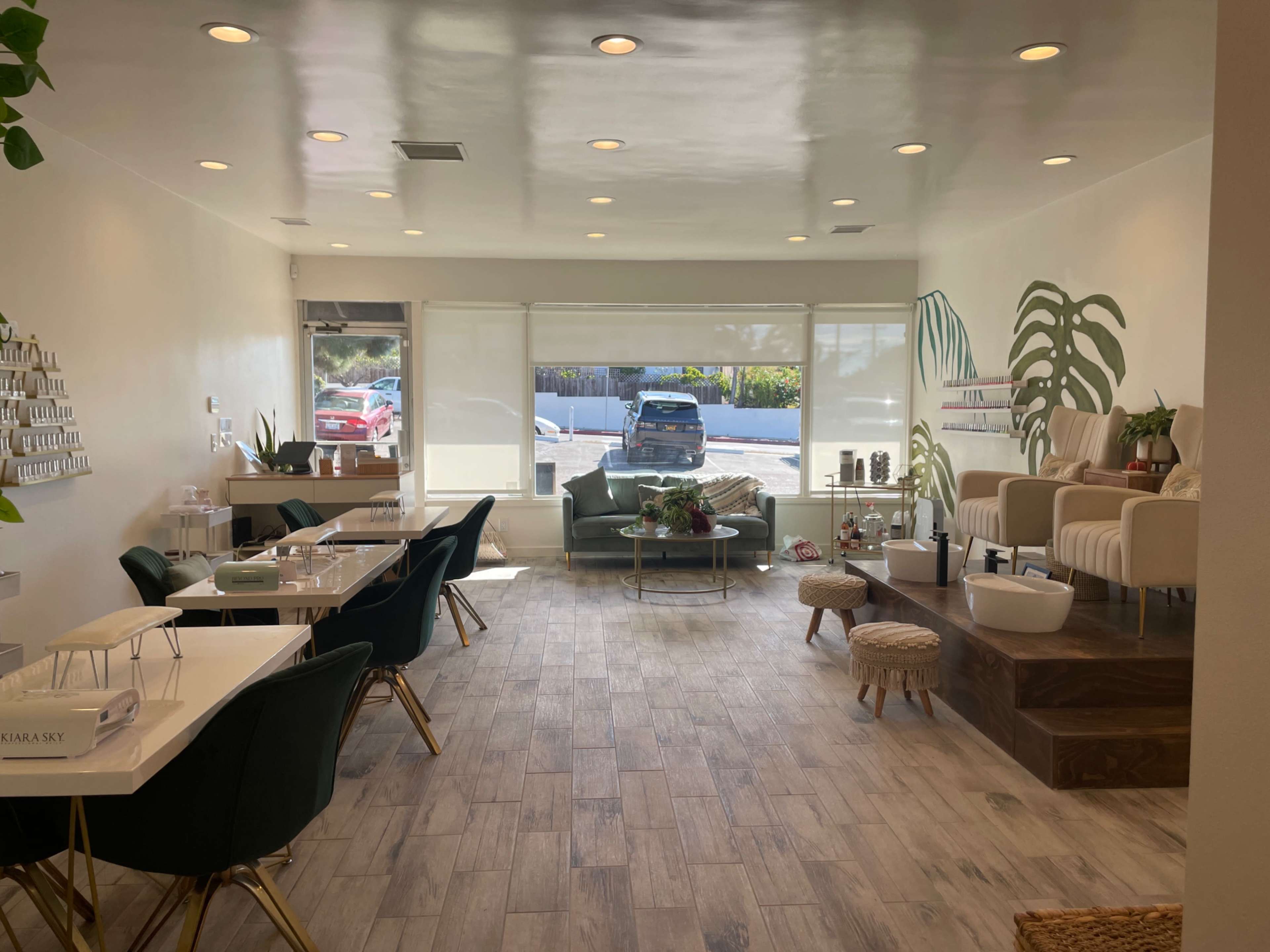 A modern interior of a wellness or beauty salon with green chairs, treatment stations, and large windows overlooking a parking area.
