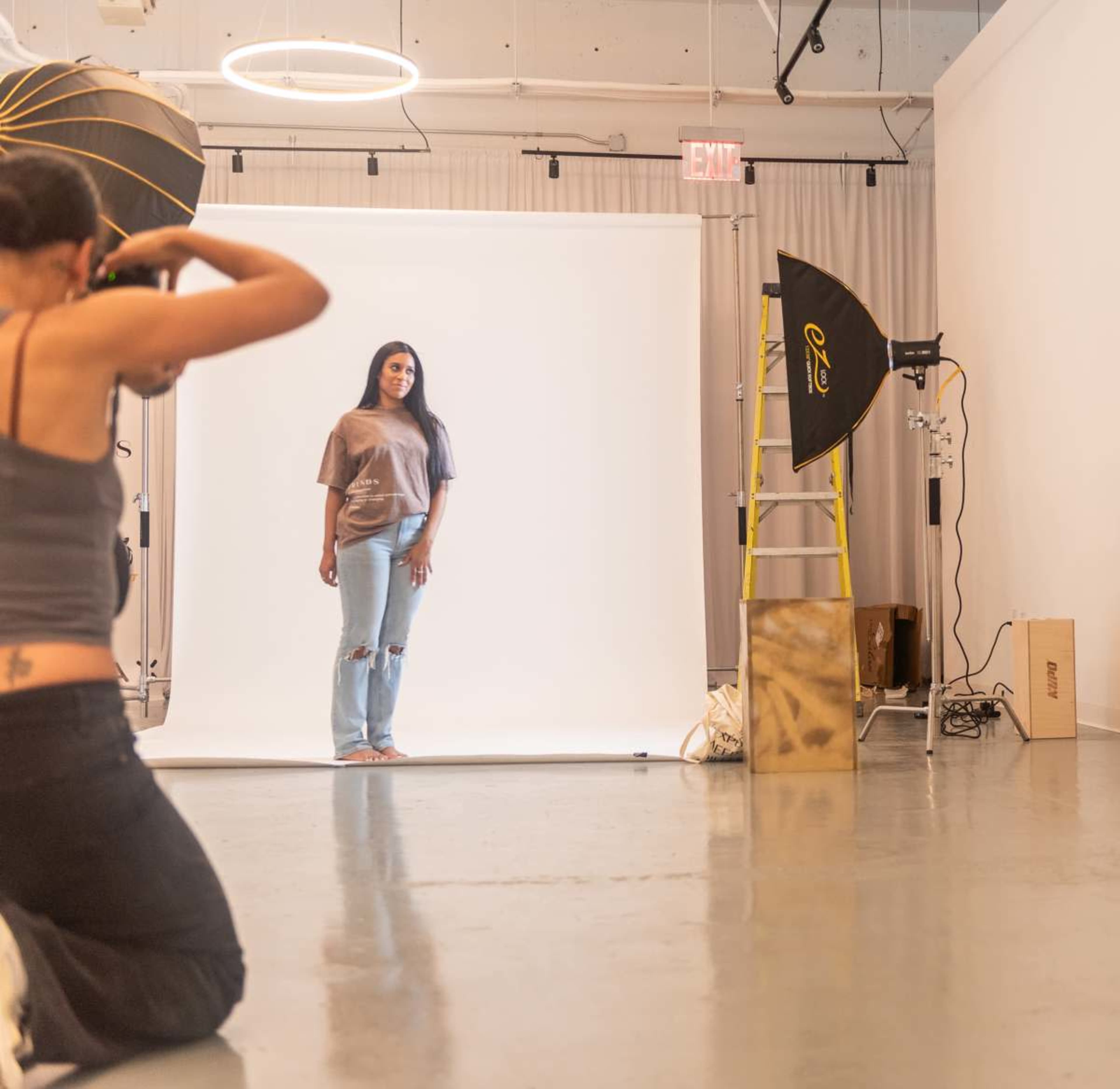 A photographer captures a model posing in front of a white backdrop in a well-lit studio.