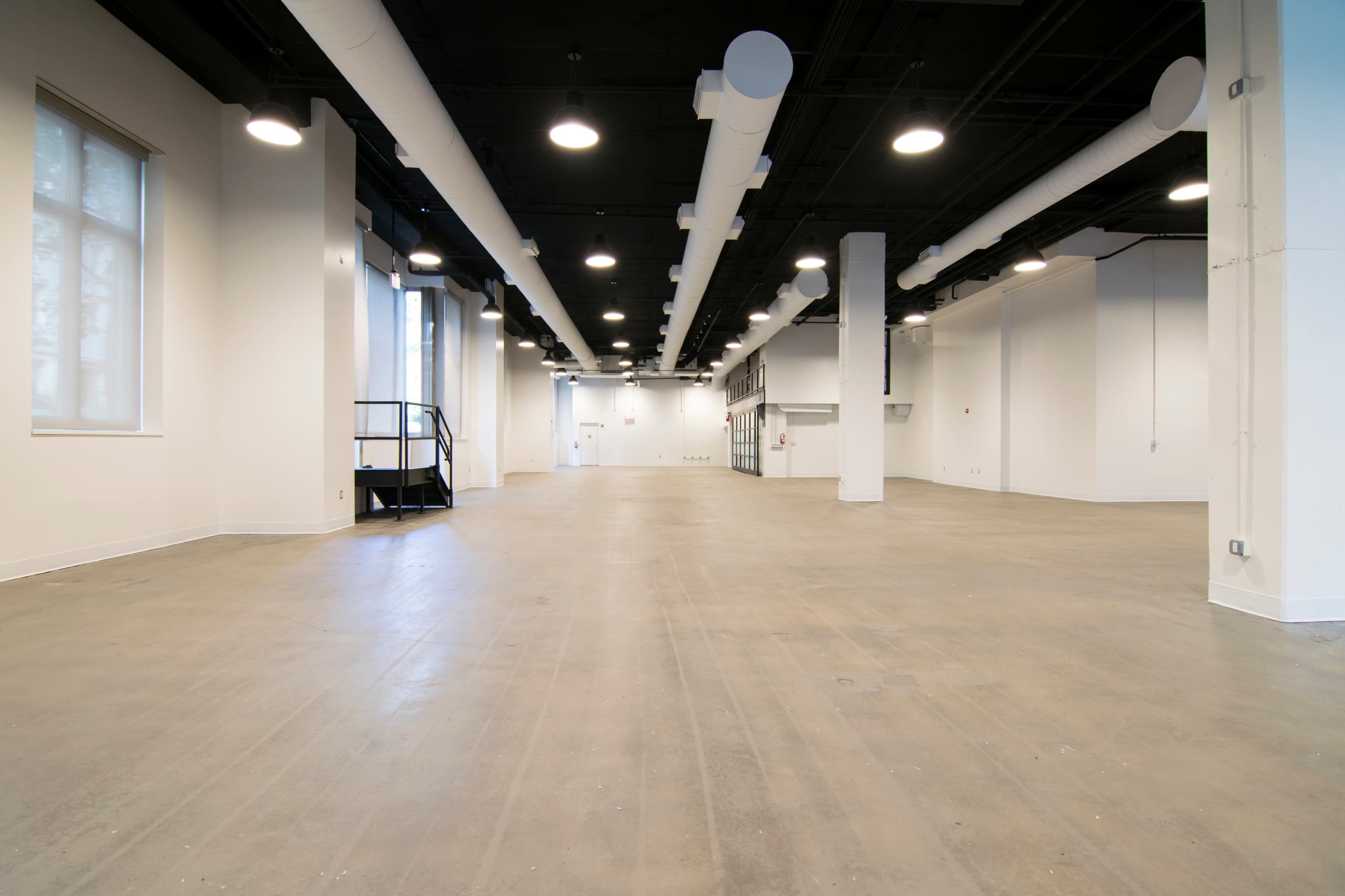 An empty commercial space with concrete floors, white walls, and exposed ductwork.