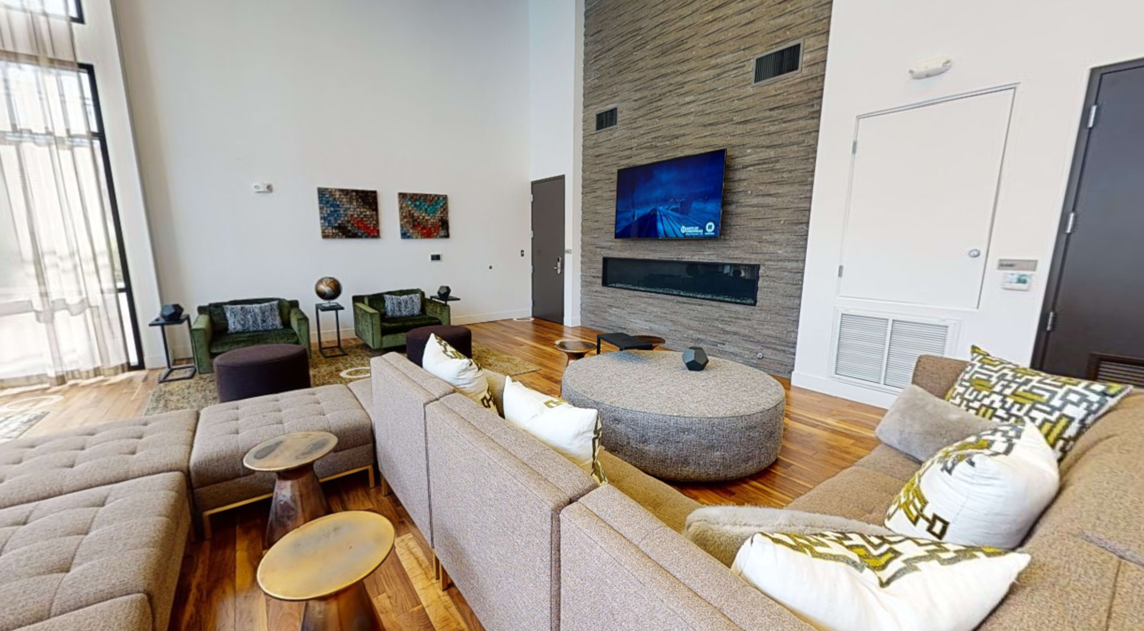 A modern living room features a large sectional sofa, a circular coffee table, and a wall-mounted television above a sleek fireplace.
