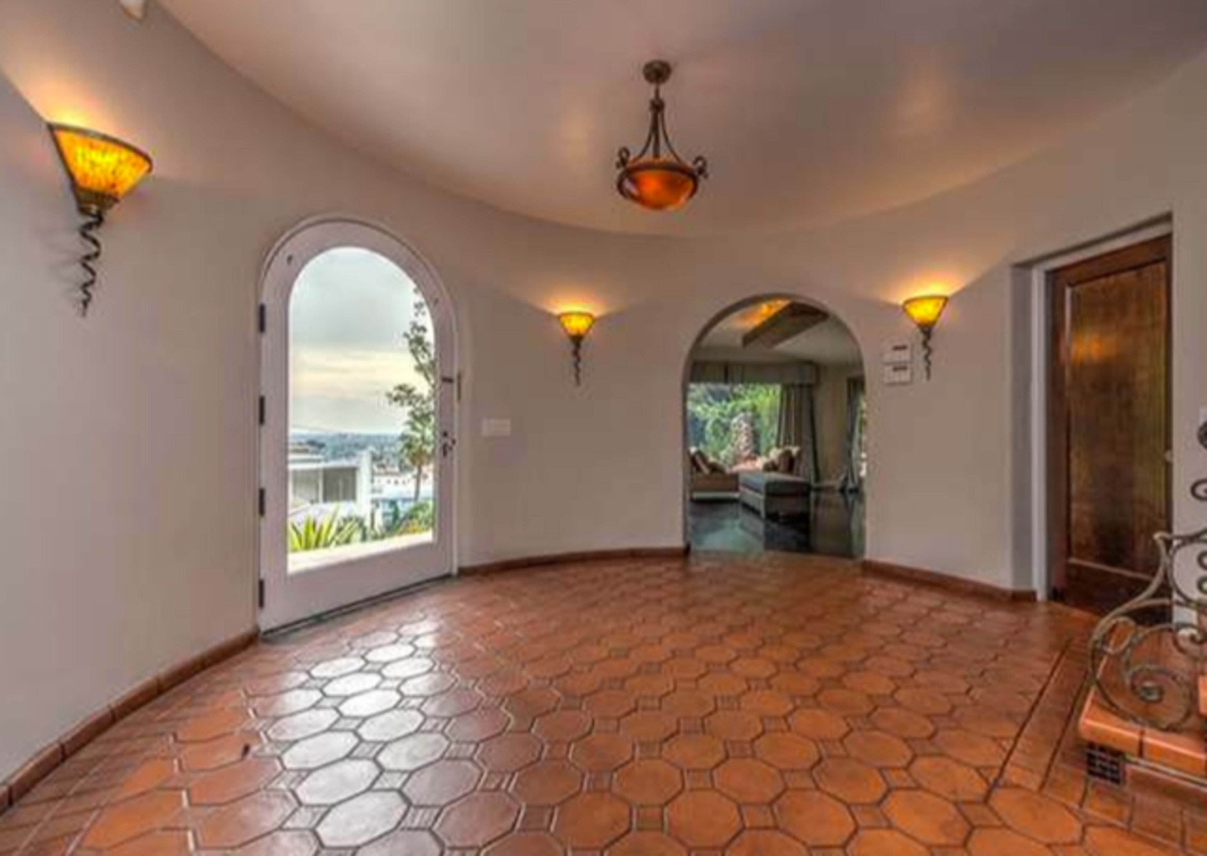 The image shows a round entryway with hexagonal terracotta tiles, arched doorways, and decorative wall sconces.