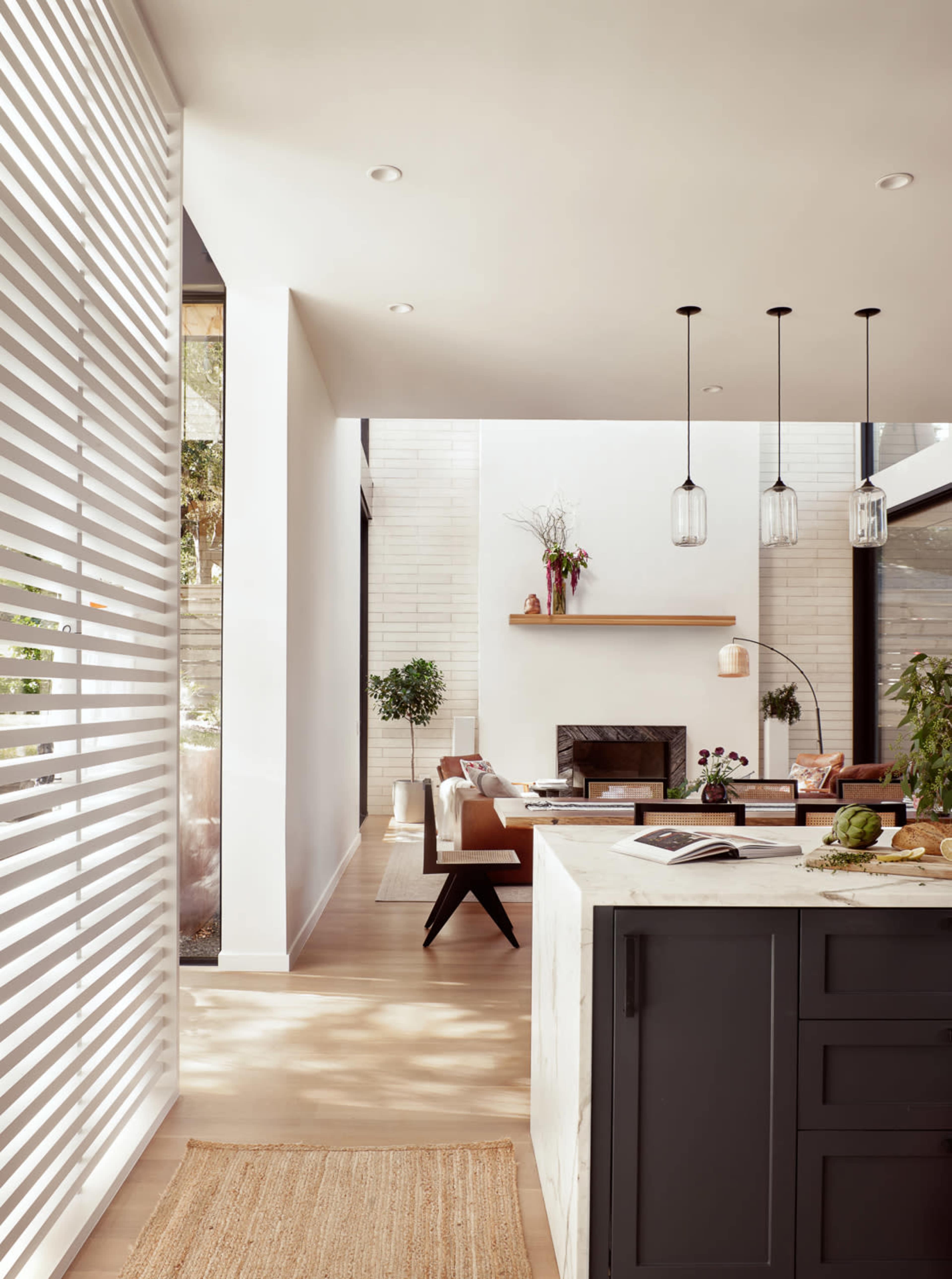 The image shows a modern living space with a kitchen, a seating area, and large windows allowing natural light to enter.