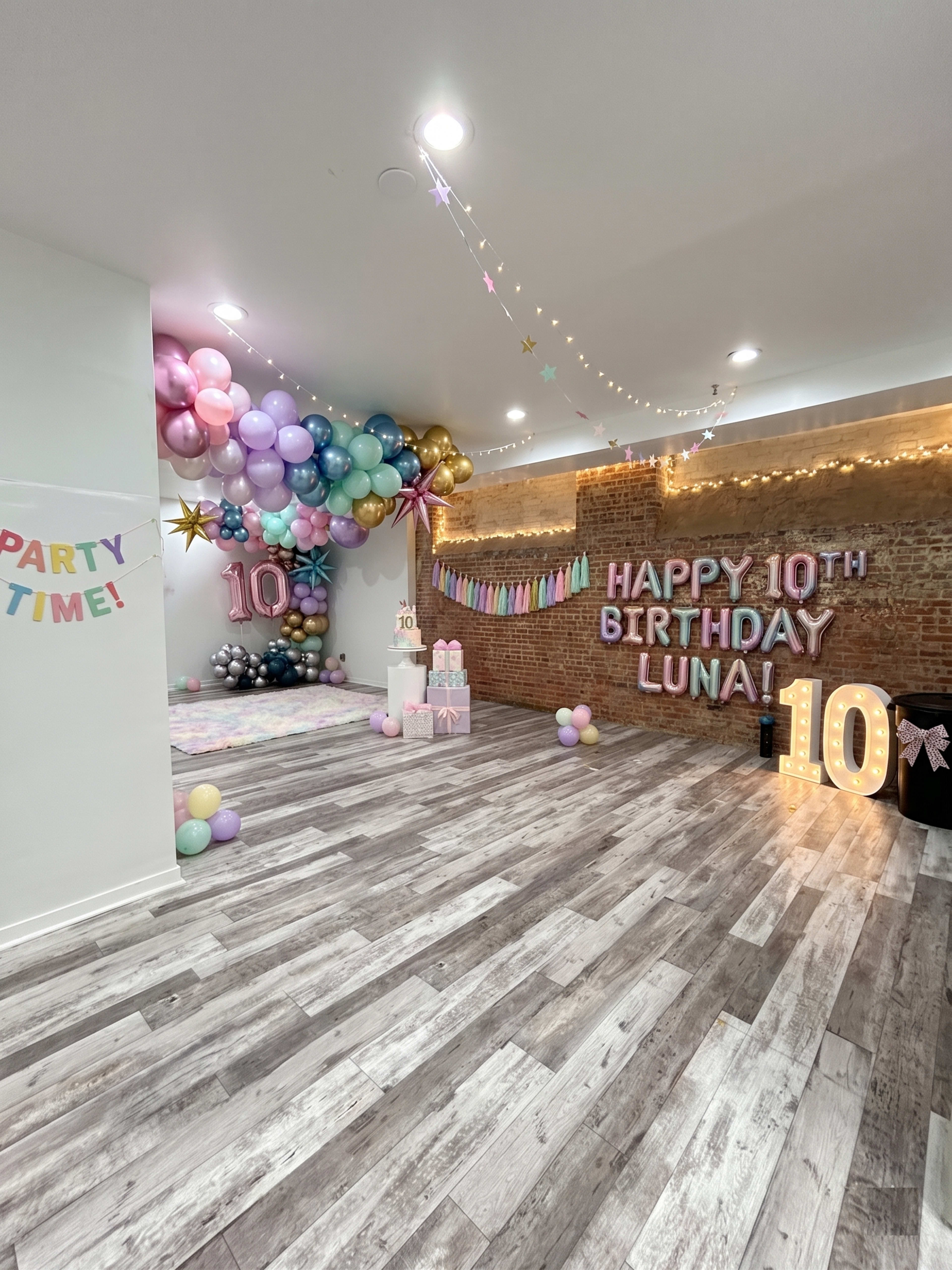 The image shows a festive birthday party setup featuring colorful balloons, a "Happy 10th Birthday Luna!" banner, and decorative lights in a room with wooden flooring.
