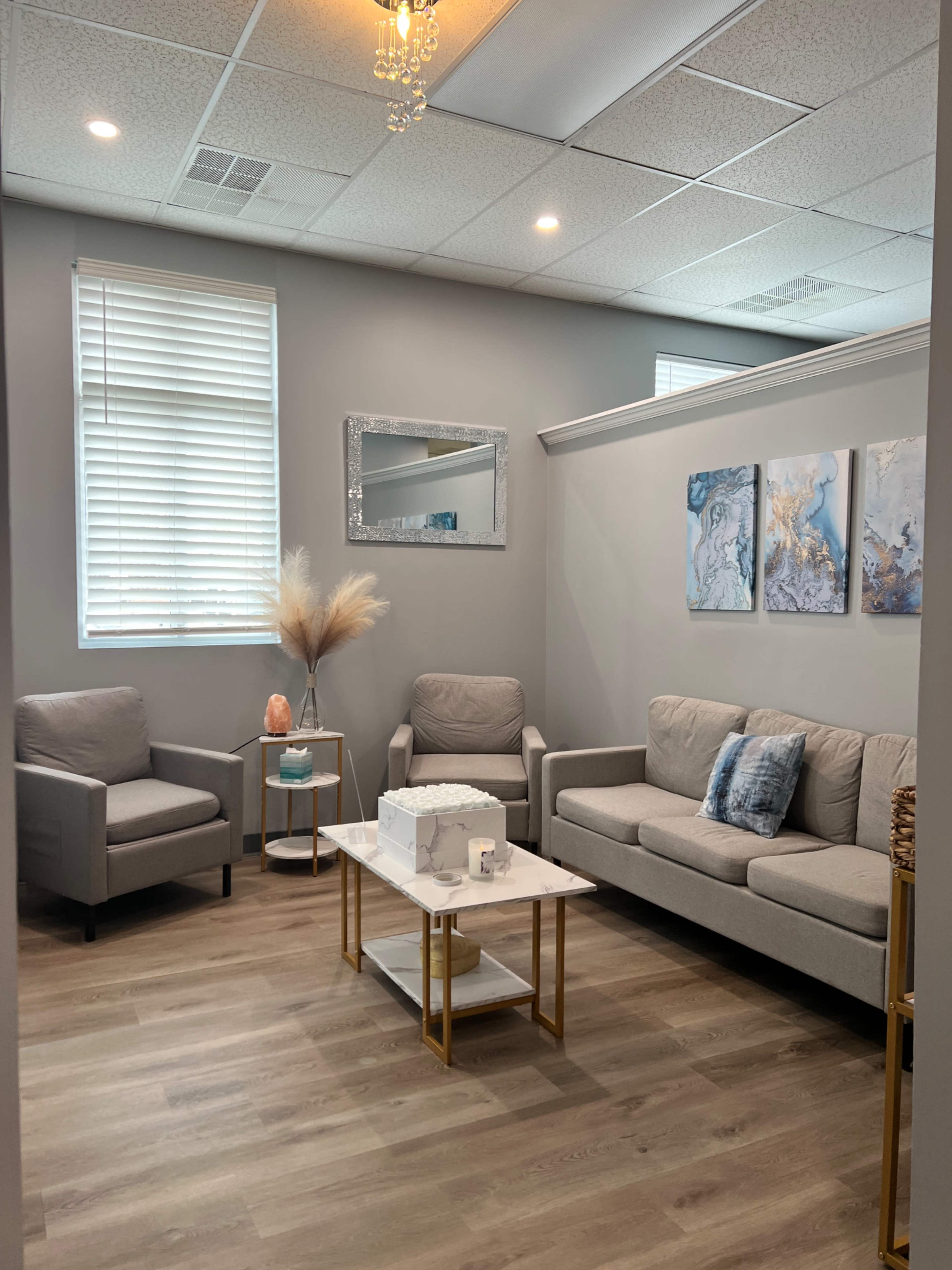 A modern waiting room features gray sofas and armchairs, a marble coffee table, and abstract artwork on the walls.