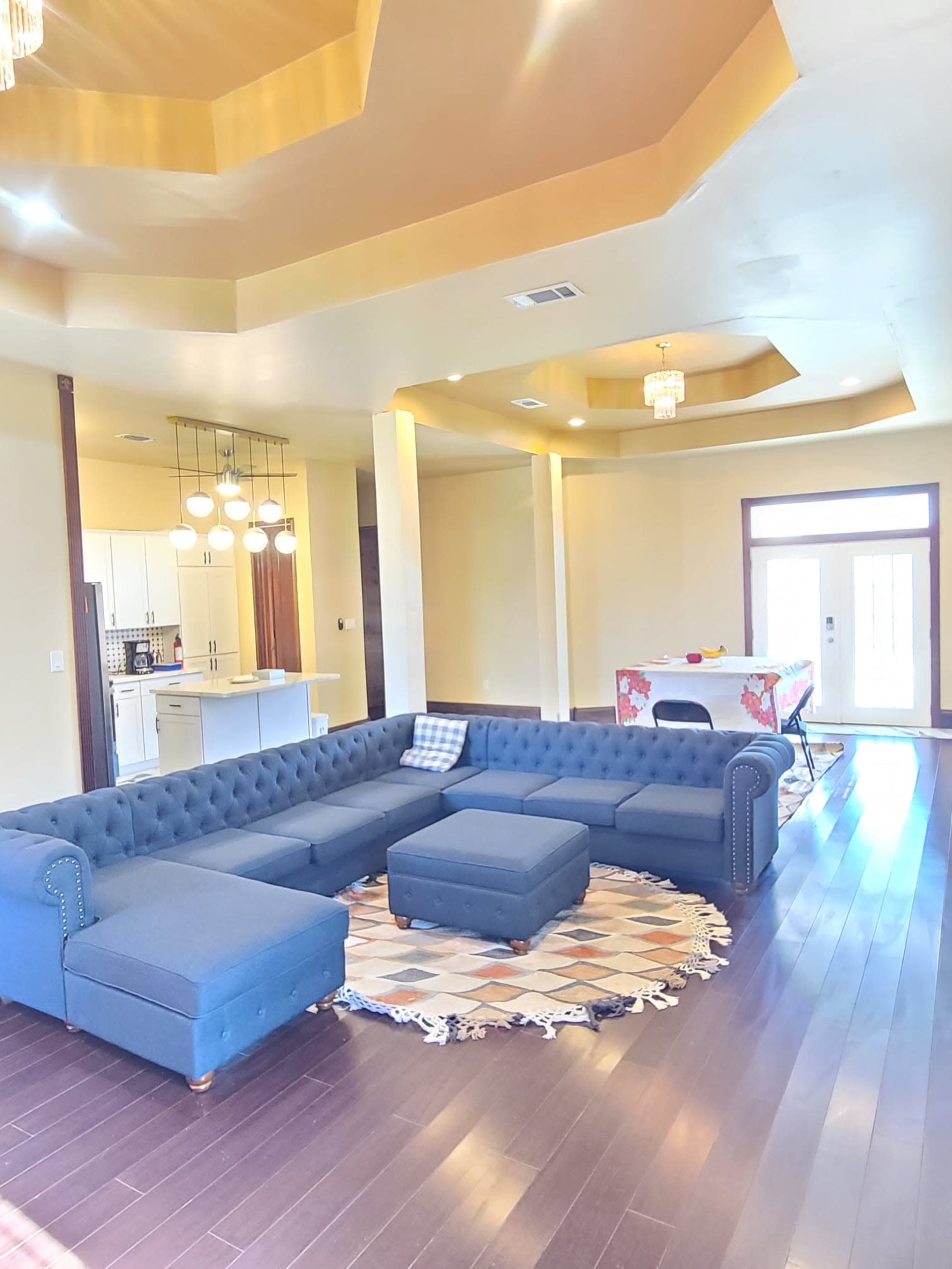 A spacious living room with a navy blue sectional sofa, a round patterned rug, and a modern dining area in the background.