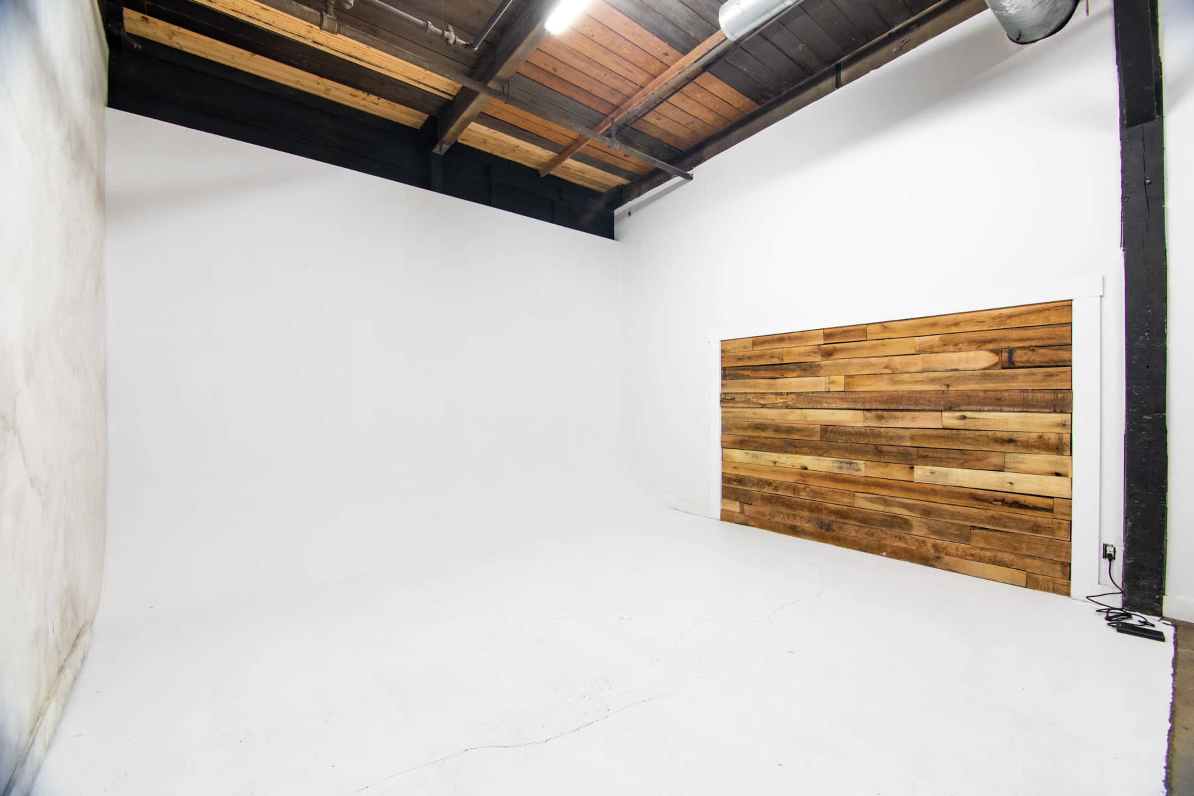 An empty photography studio with a smooth white backdrop and a wooden accent wall.