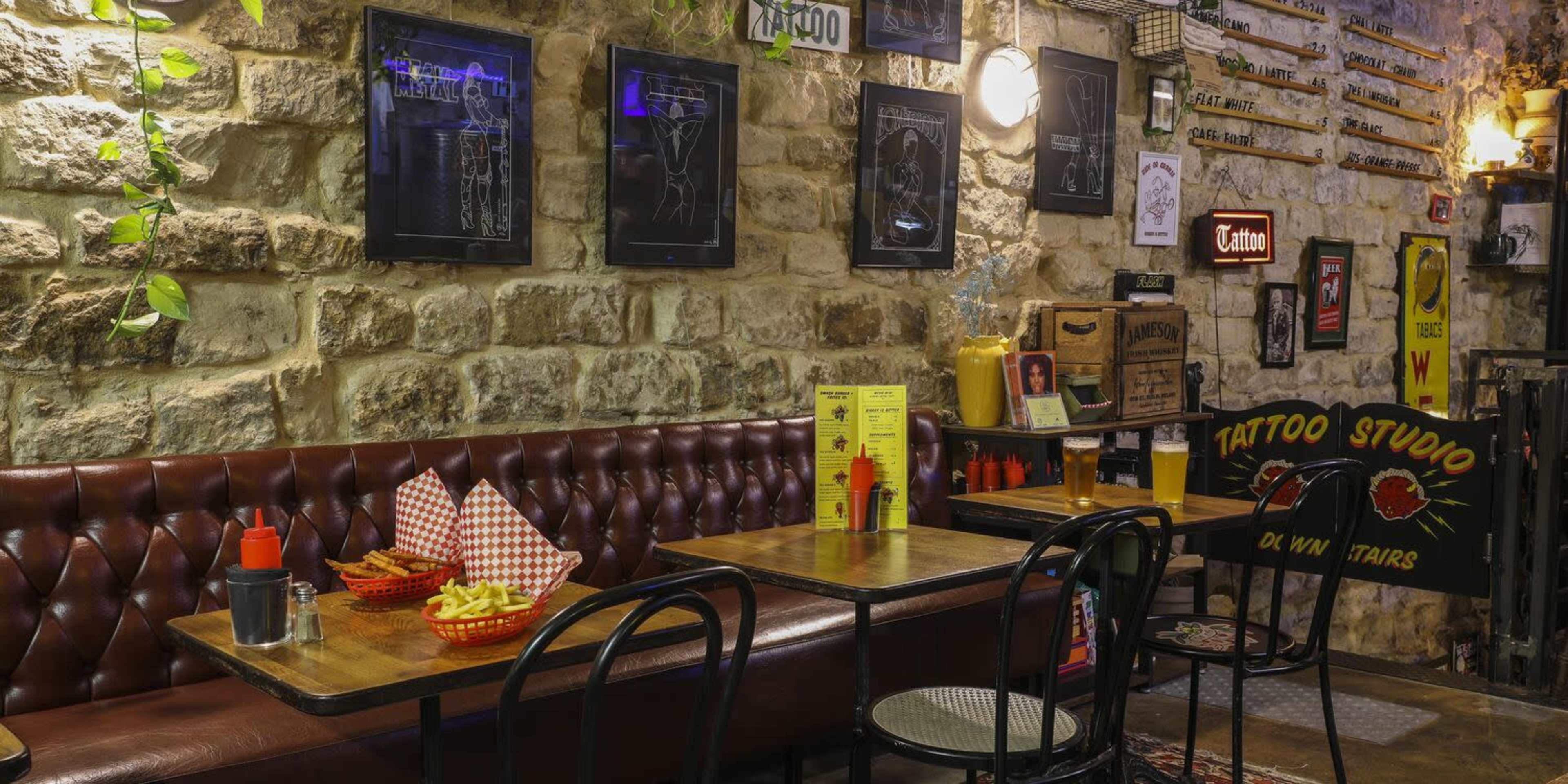 A cozy restaurant interior with stone walls, wooden tables, and a seating area featuring red leather benches, framed art, and vintage signs.