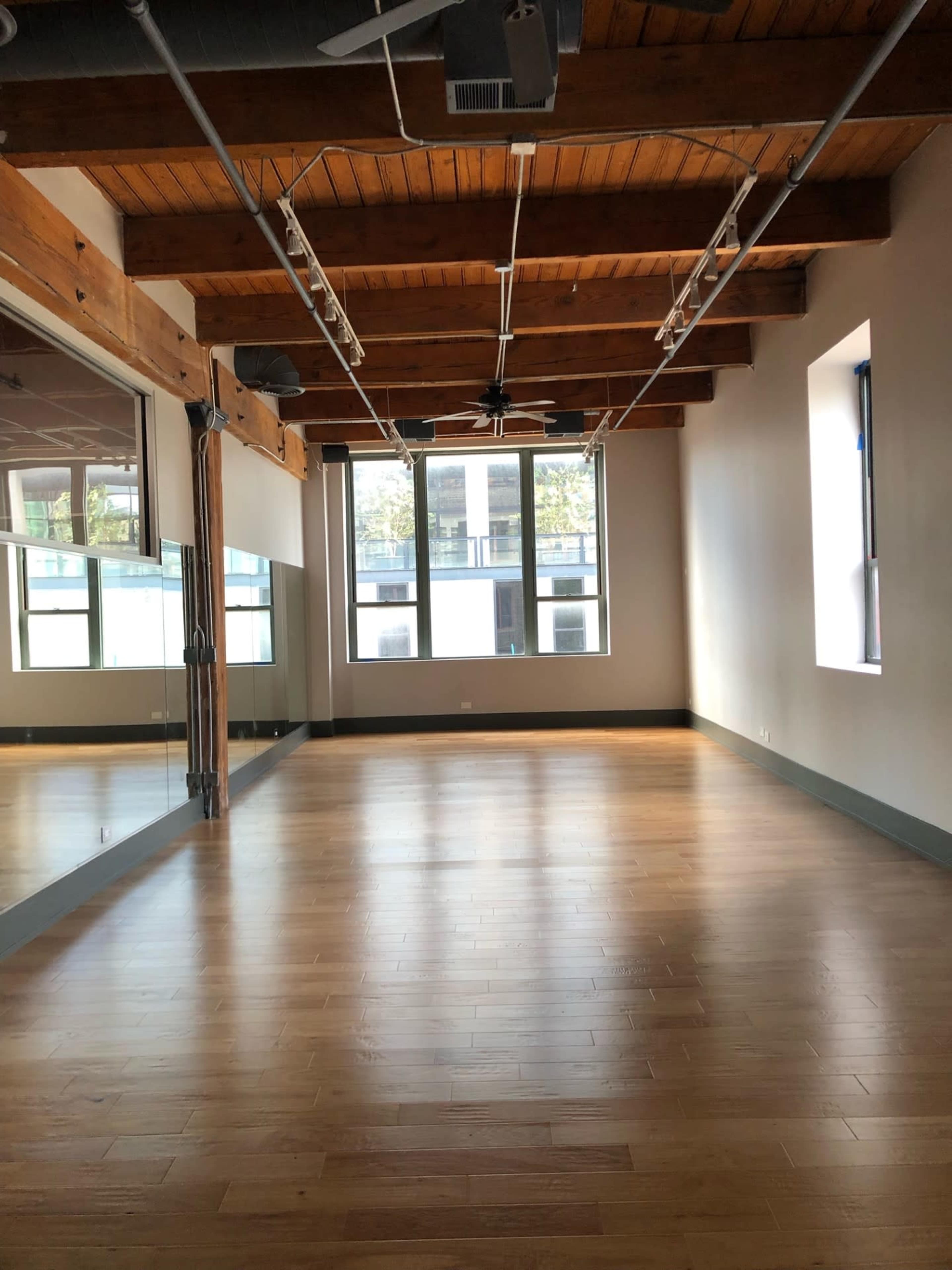 An empty room with wooden beams, hardwood flooring, and large windows reflecting natural light.