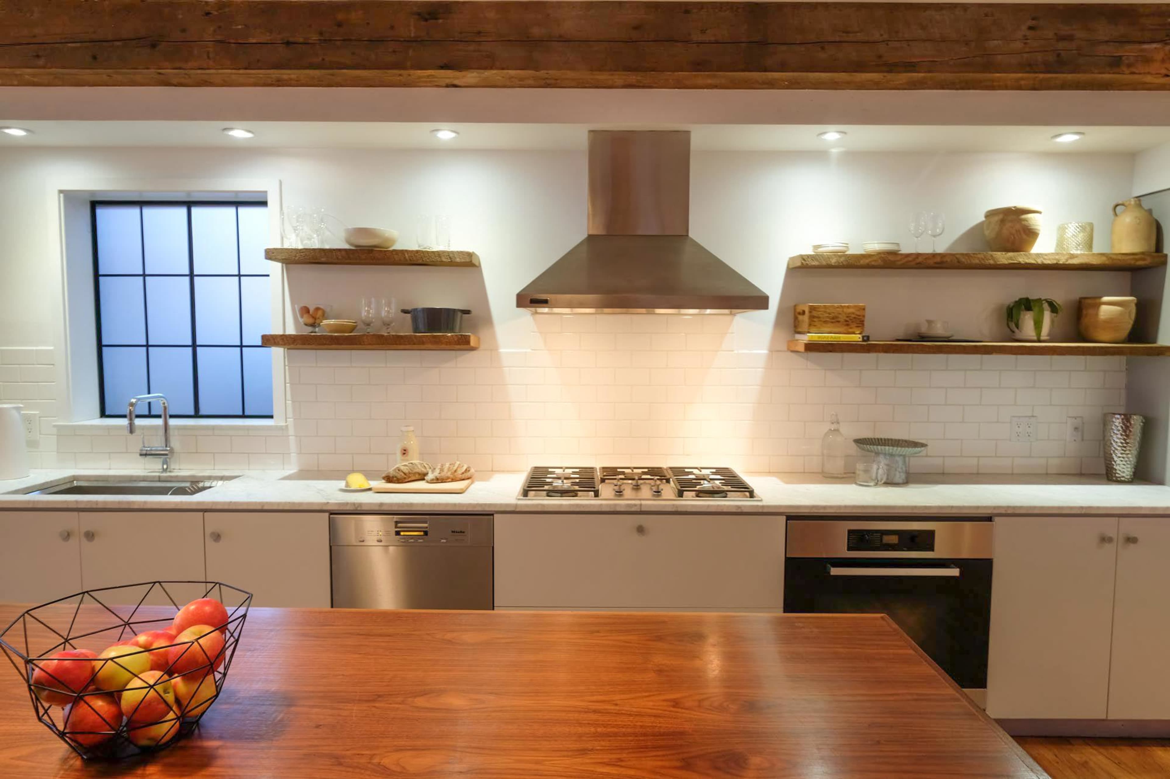 A modern kitchen features a central wooden island, stainless steel appliances, and open shelving displaying various kitchenware.