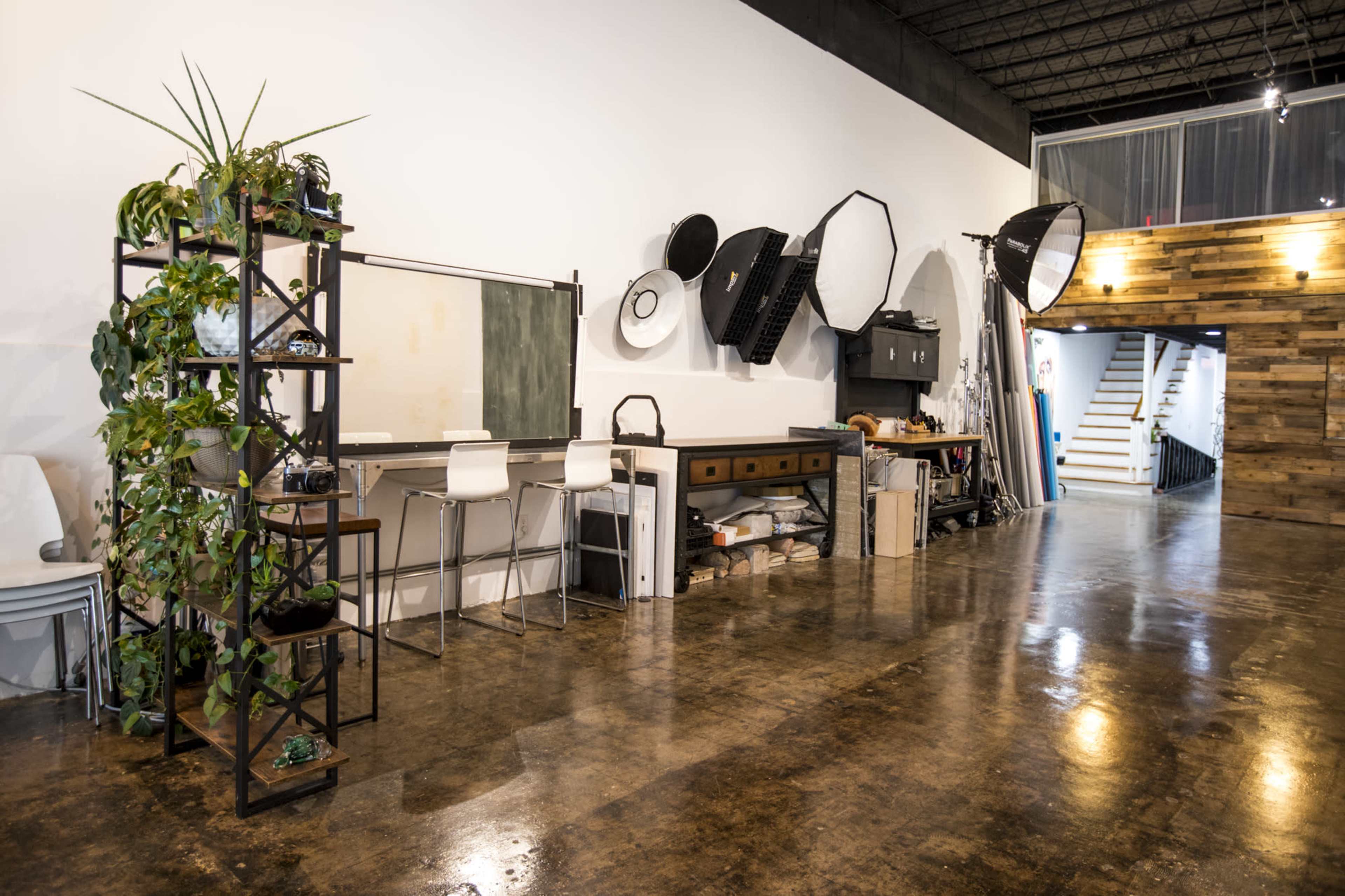 A spacious interior of a studio with a wooden floor, a black and white color scheme, and various photography equipment mounted on the wall.