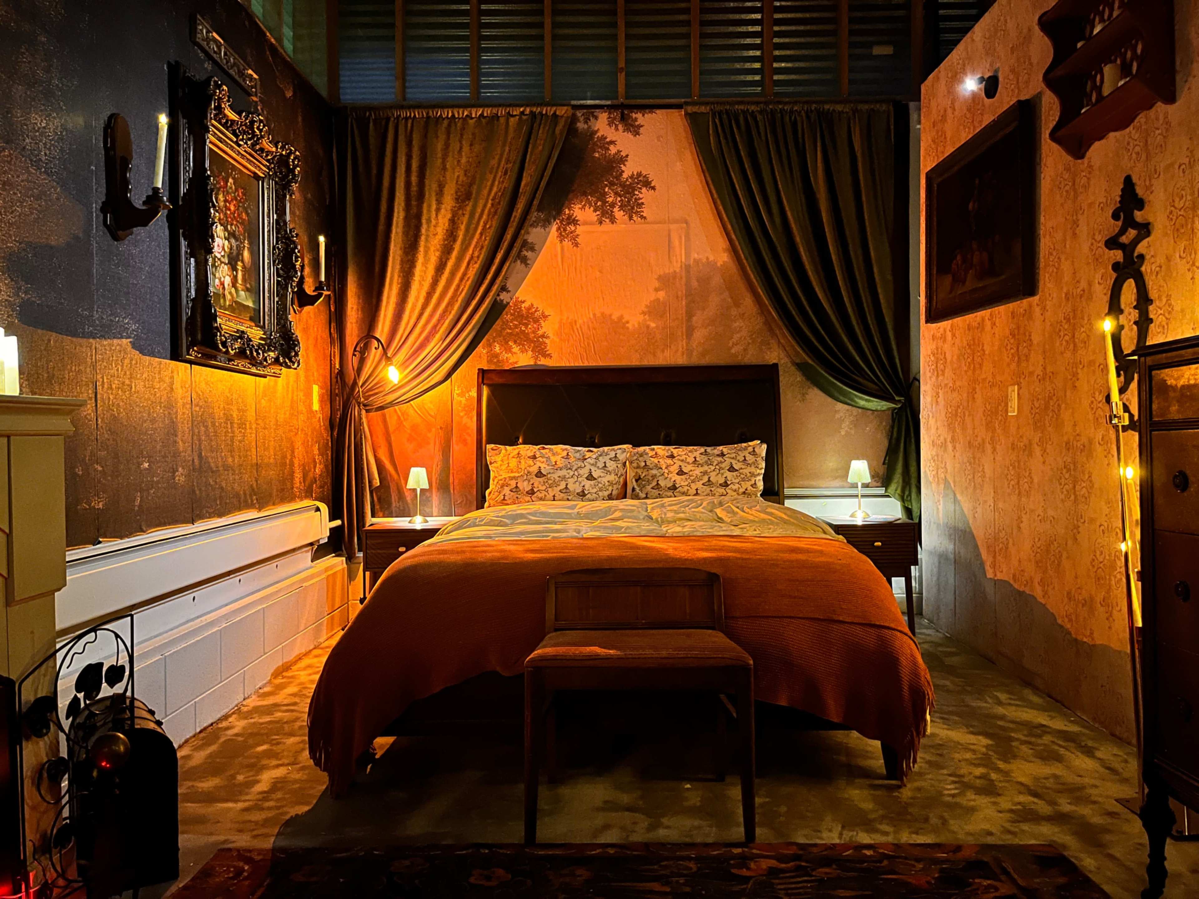 The image showcases a warmly lit bedroom featuring a large bed with patterned linens, flanked by nightstands and adorned with decorative curtains and wall art.