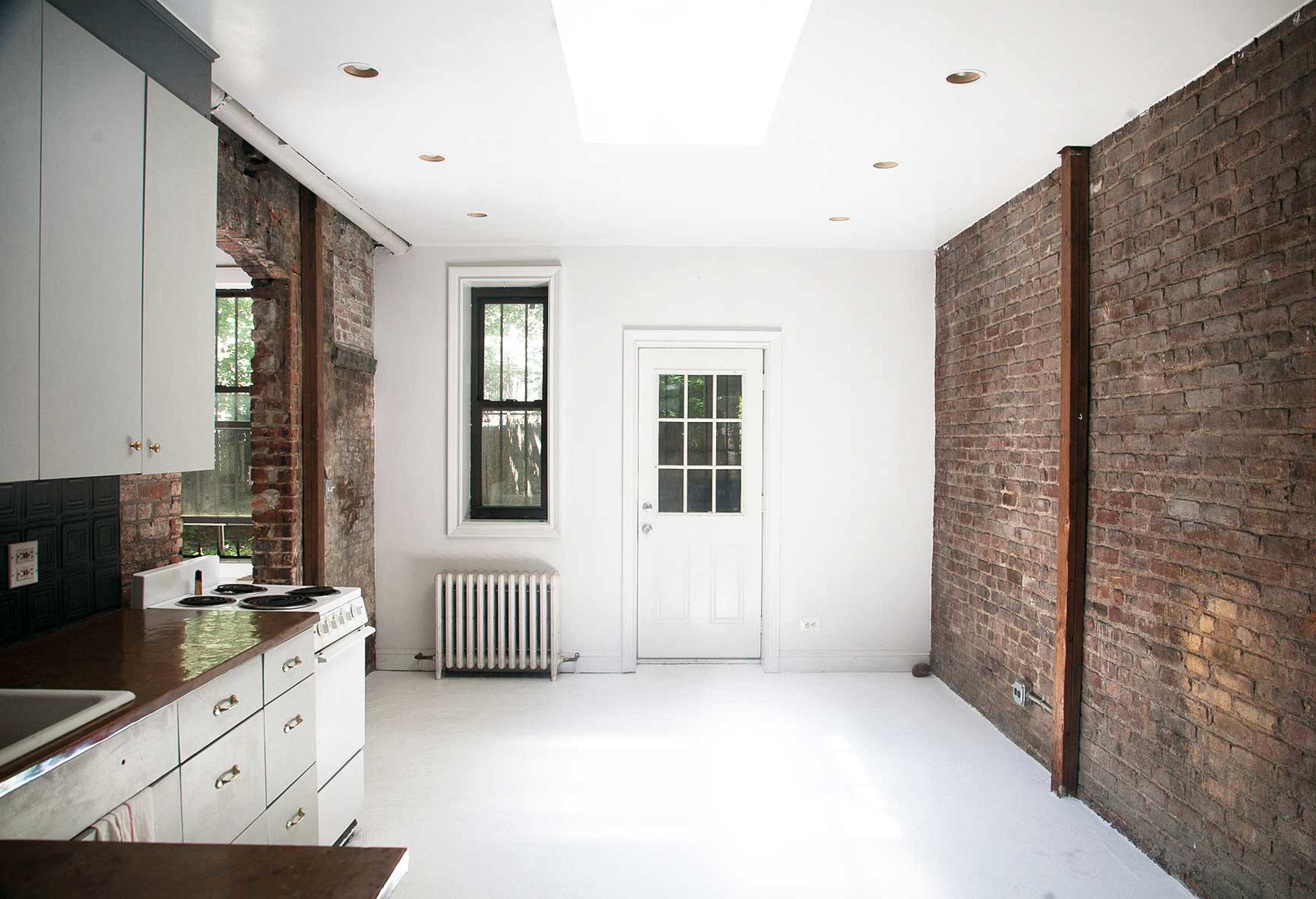 A minimalist kitchen and living area with exposed brick walls, a white ceiling, and a door leading outside.