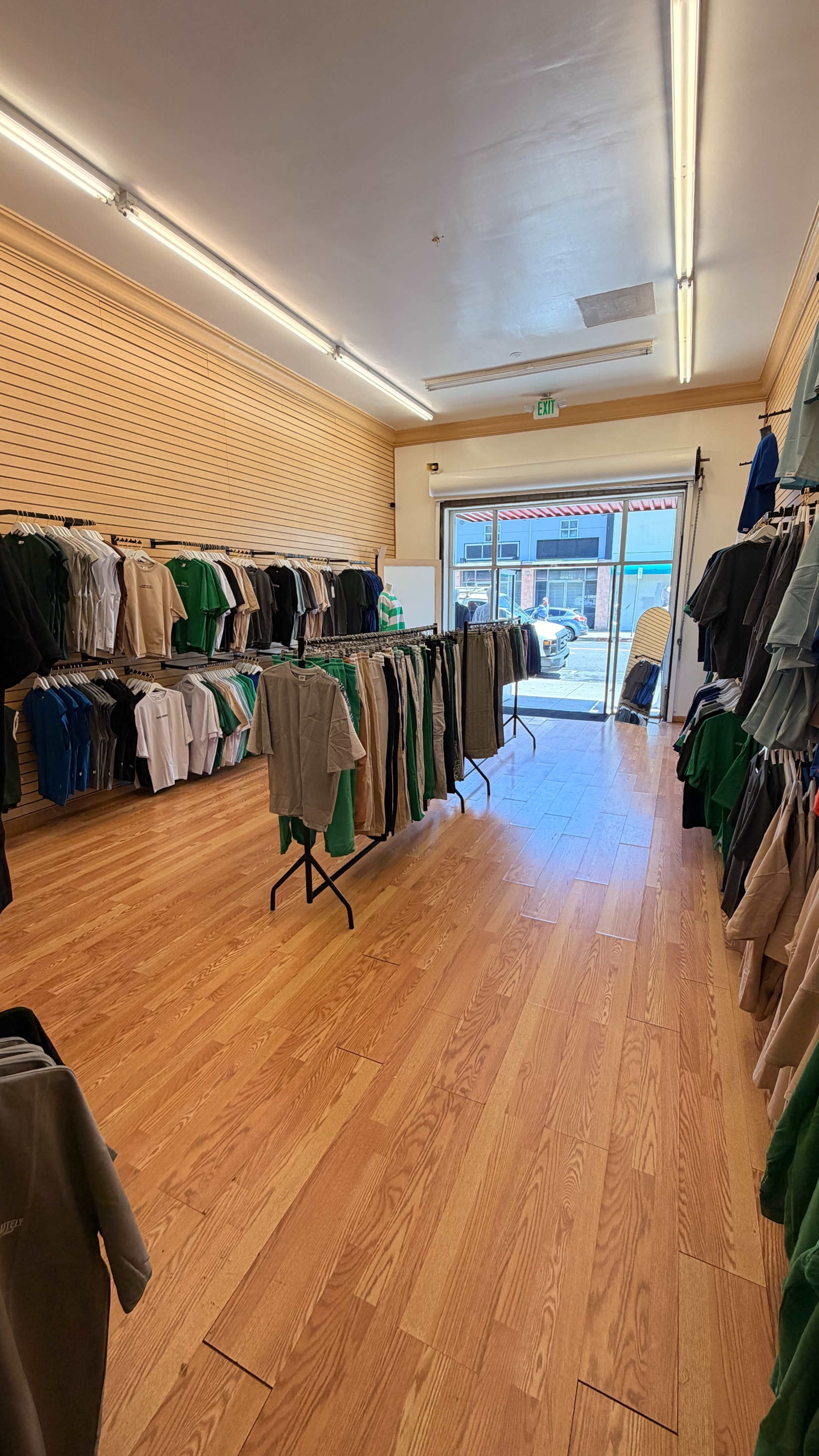 The image shows the interior of a retail store with clothing racks displaying various apparel, and a large entrance door leading to the outside.