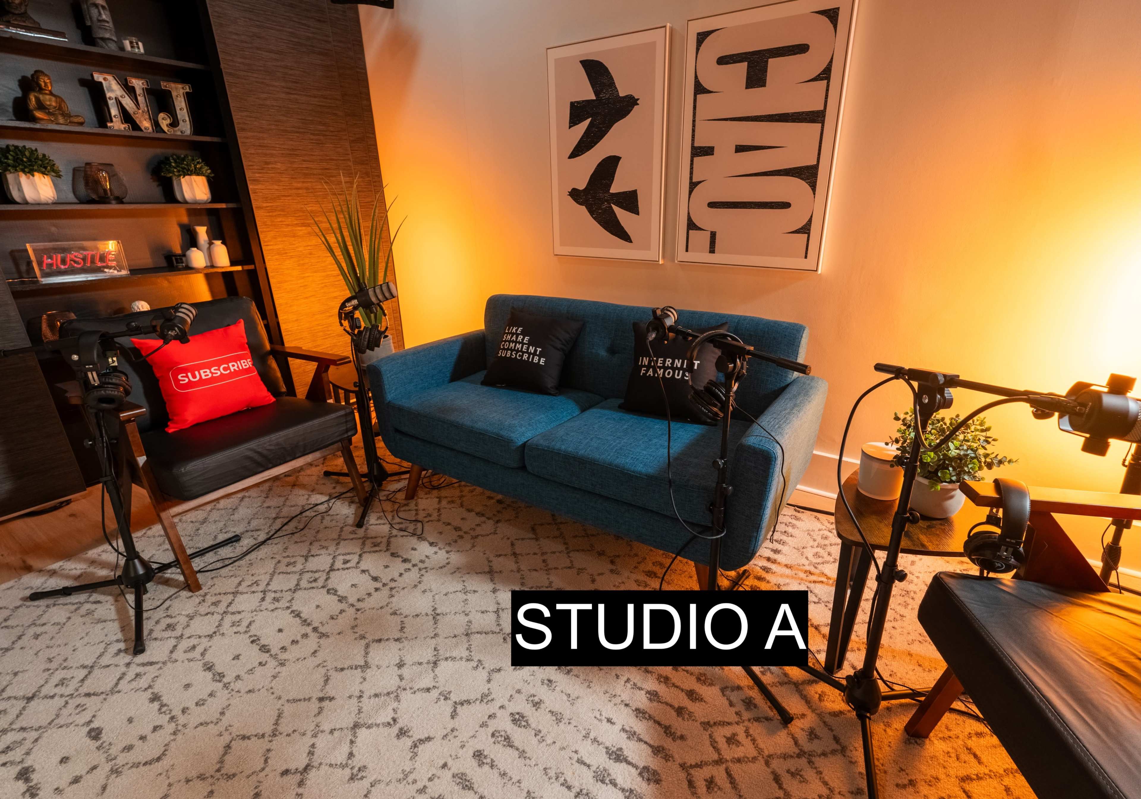 The image shows a small recording studio with a blue couch, a chair, and microphone stands arranged around a patterned rug and illuminated by warm lighting.