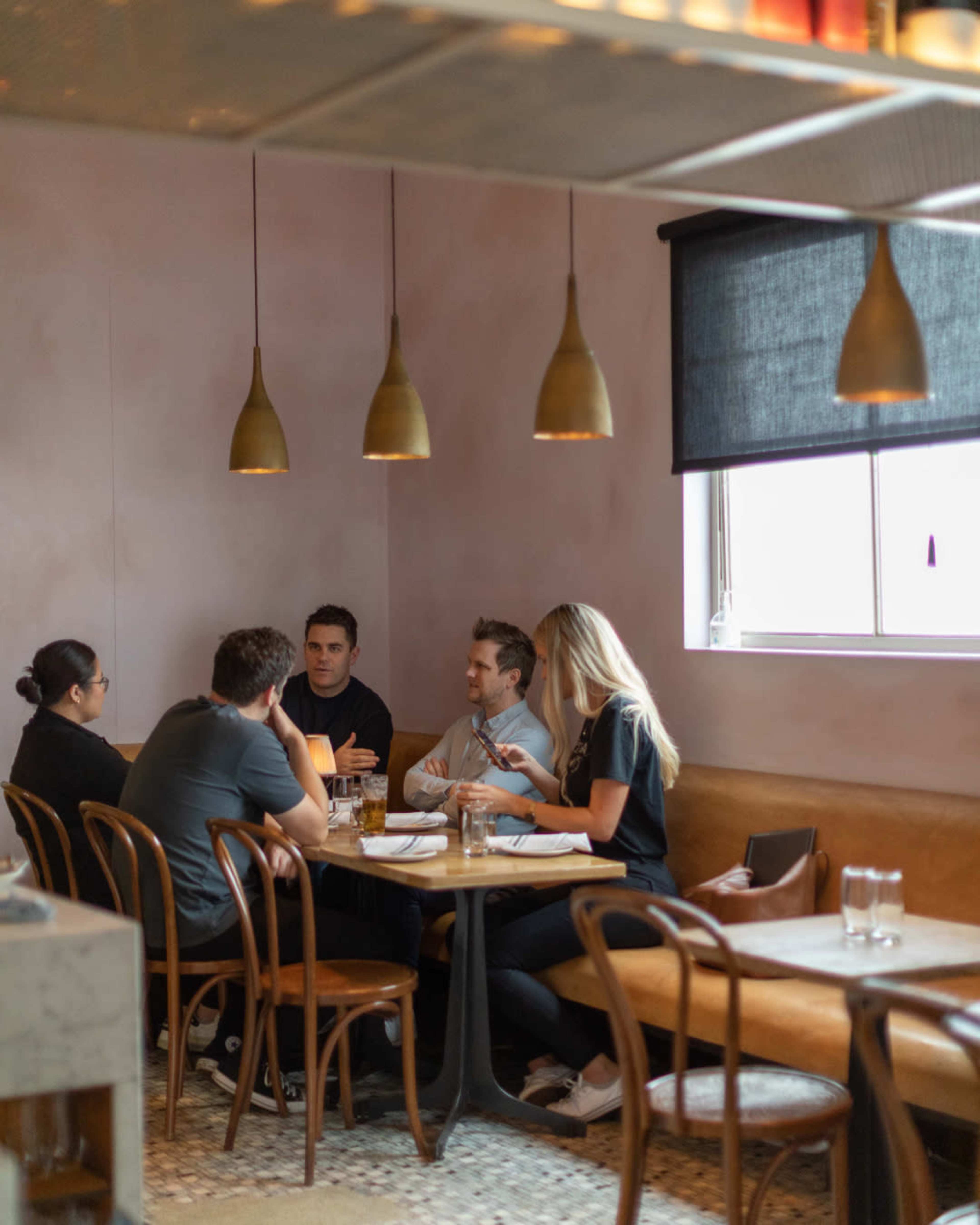 A group of five people sits around a table in a restaurant, engaged in conversation under pendant lights.