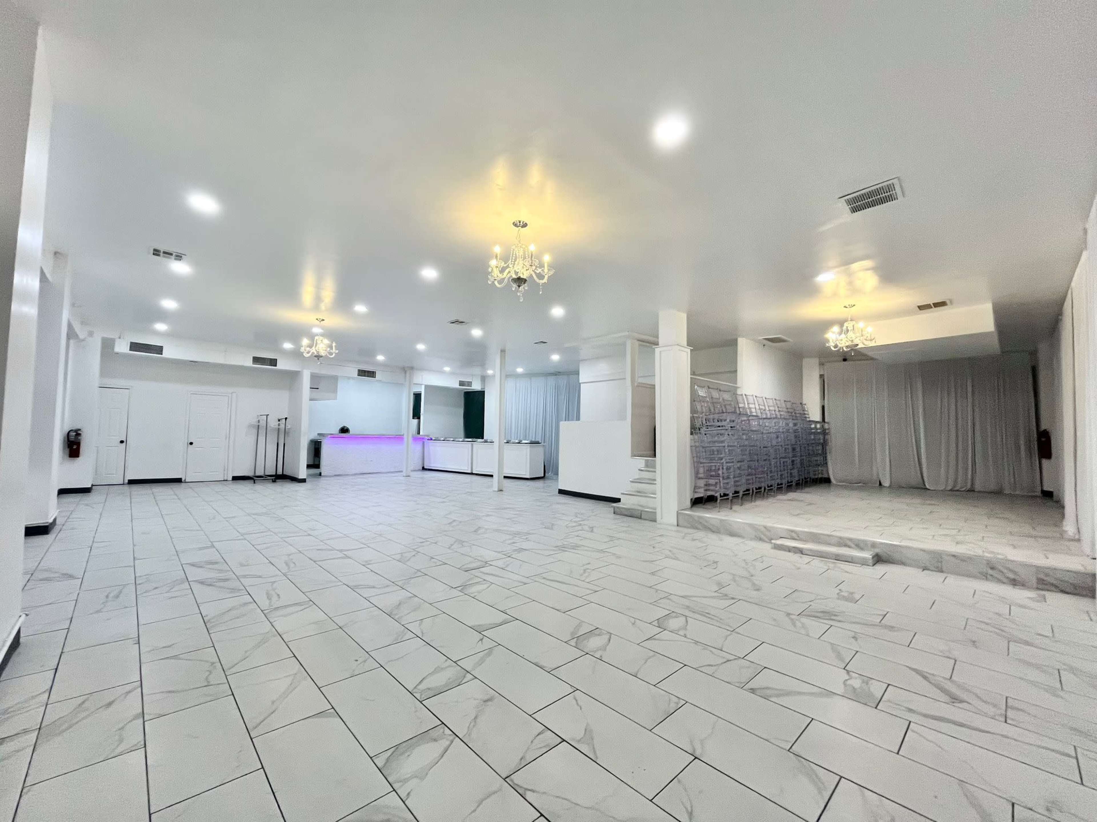 A spacious, well-lit open area with tiled flooring, a reception counter, and a section with white draping in the background.