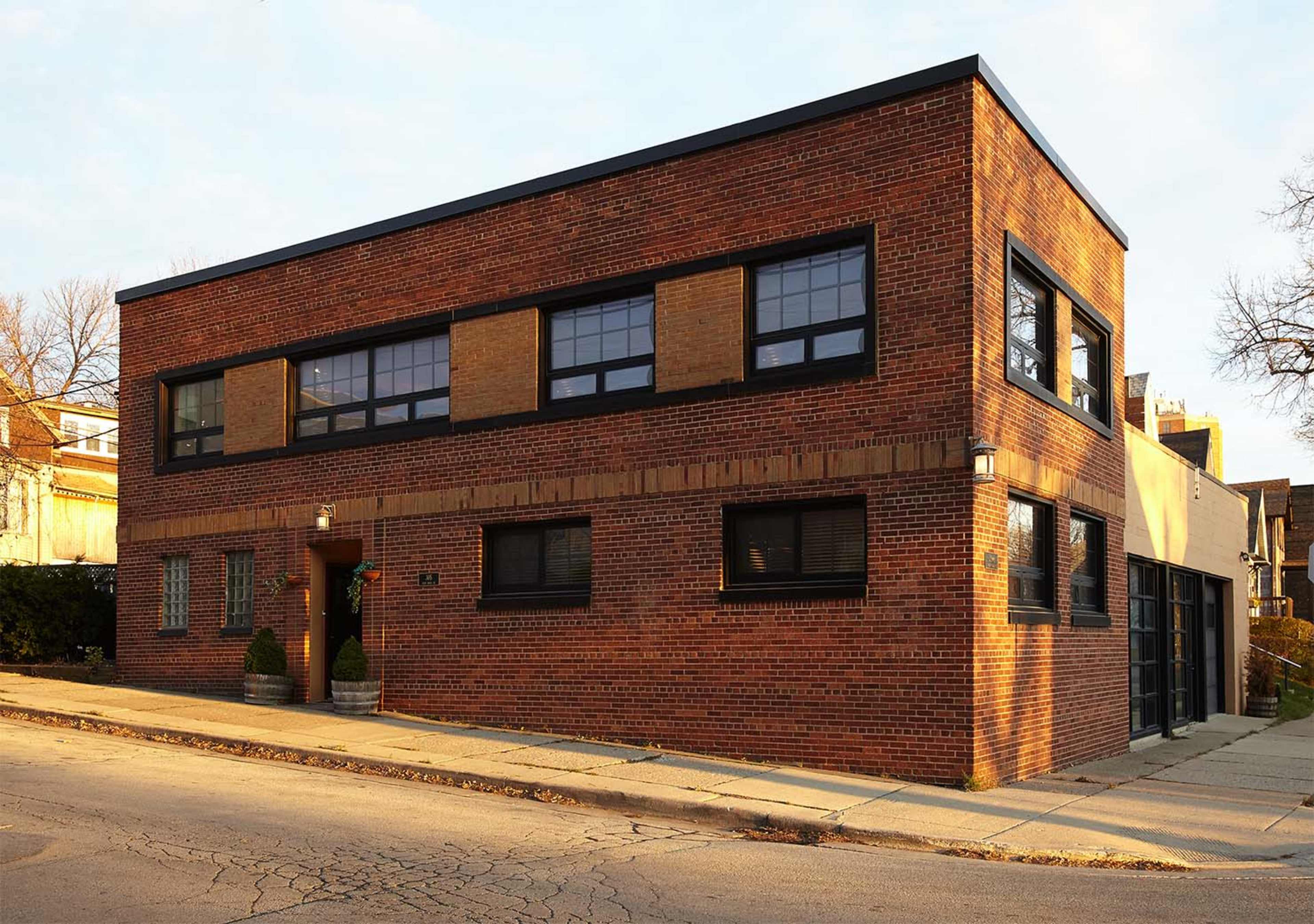A large, modern brick building with large windows and a flat roof is situated at the corner of a city street.