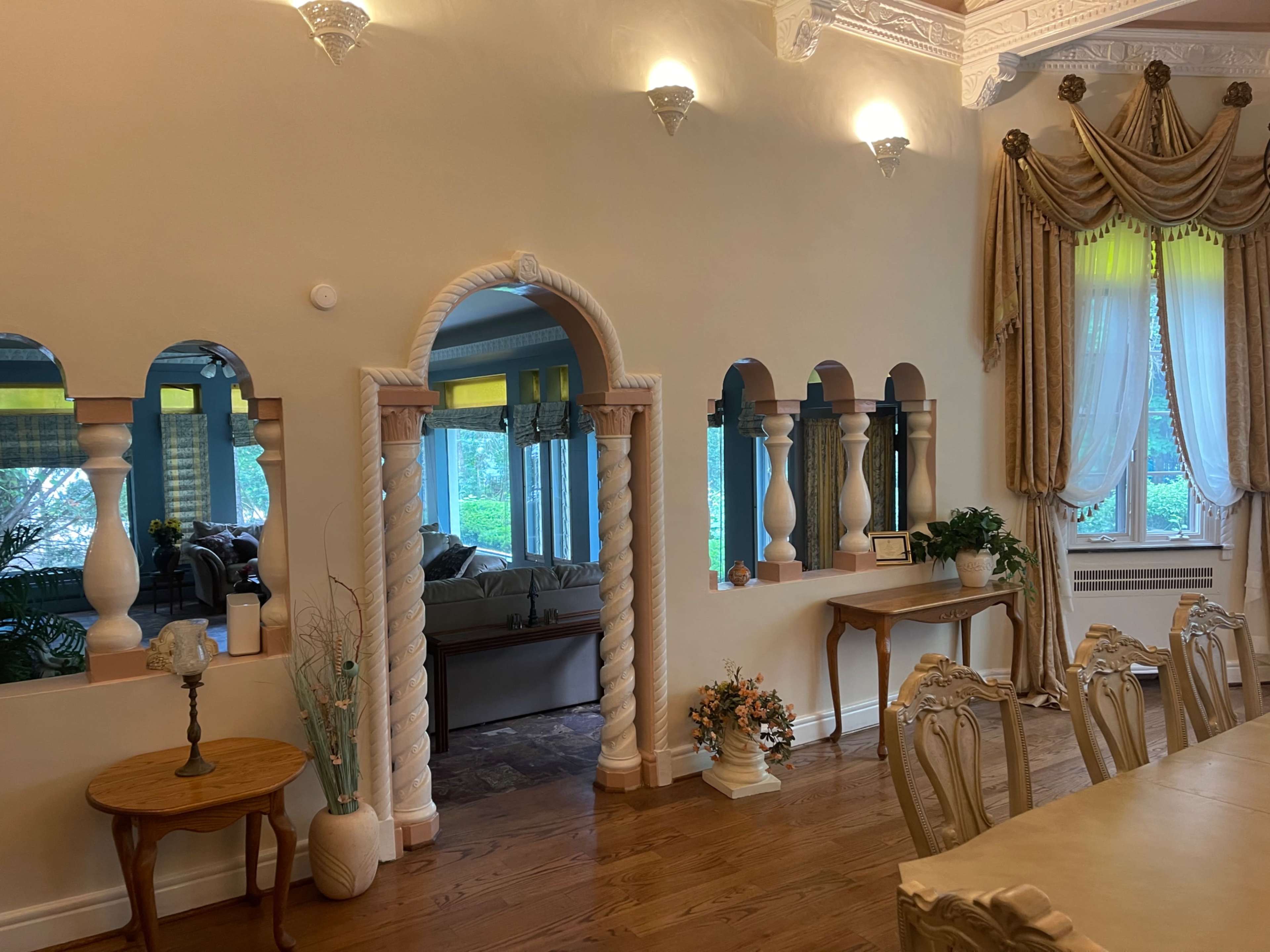 The image shows a dining area with elegantly designed arches and columns, leading to a well-lit living space beyond.